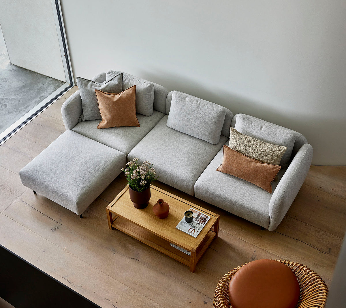 A stylish light gray sectional sofa with pillows, paired with a wooden coffee table and a round seating option, creating a cozy atmosphere.