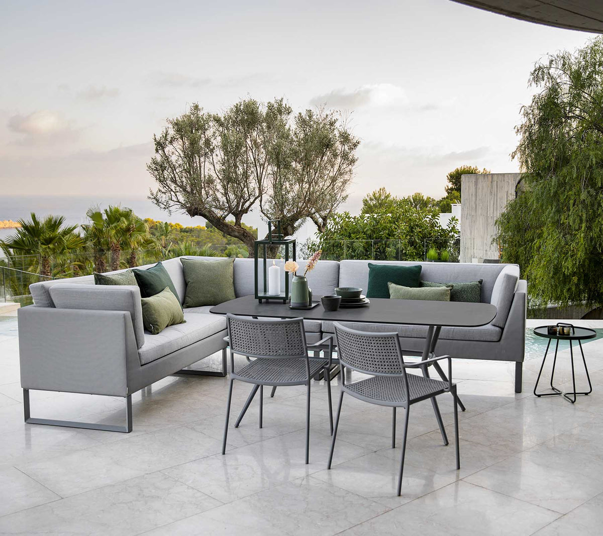 Modern outdoor seating area featuring a stylish sectional sofa, a dining table, and metal chairs surrounded by greenery.