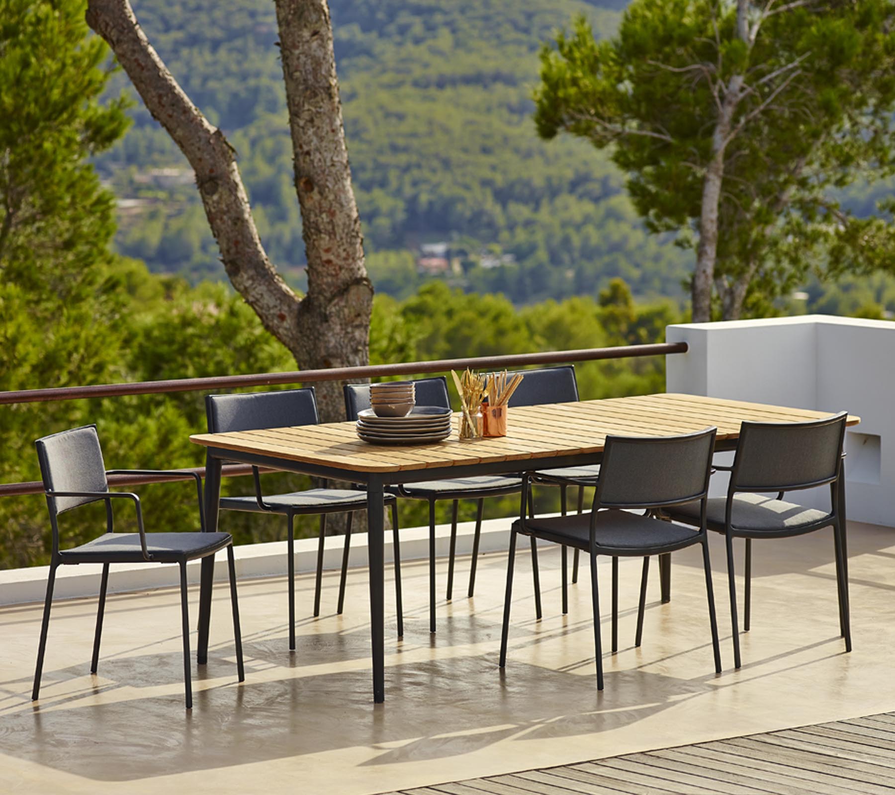 Outdoor dining table set featuring a rectangular wooden tabletop and black chairs, surrounded by greenery and scenic views.