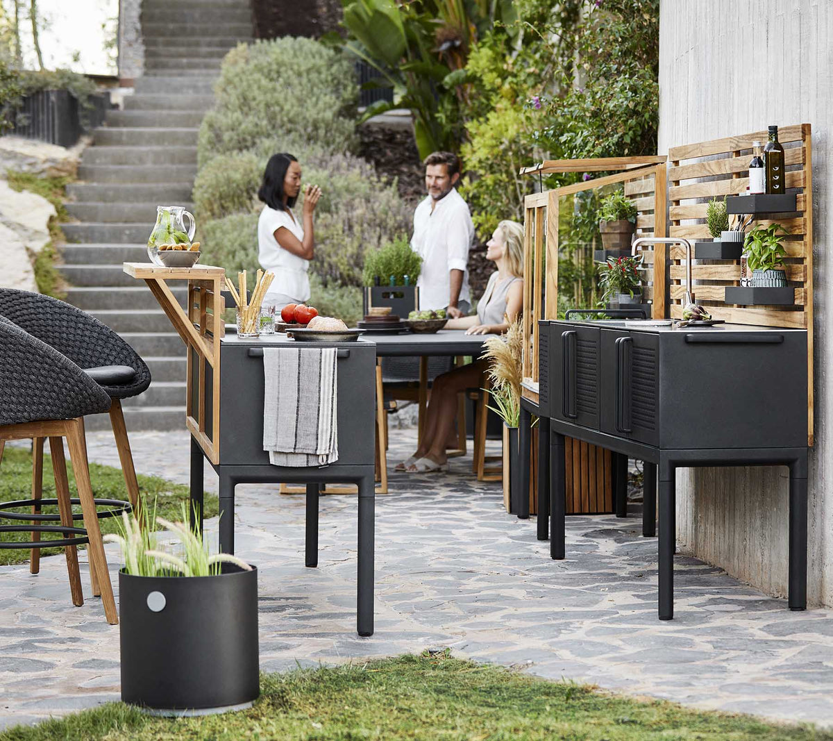 A modern outdoor dining area featuring stylish black furniture, greenery, and people enjoying a meal together.