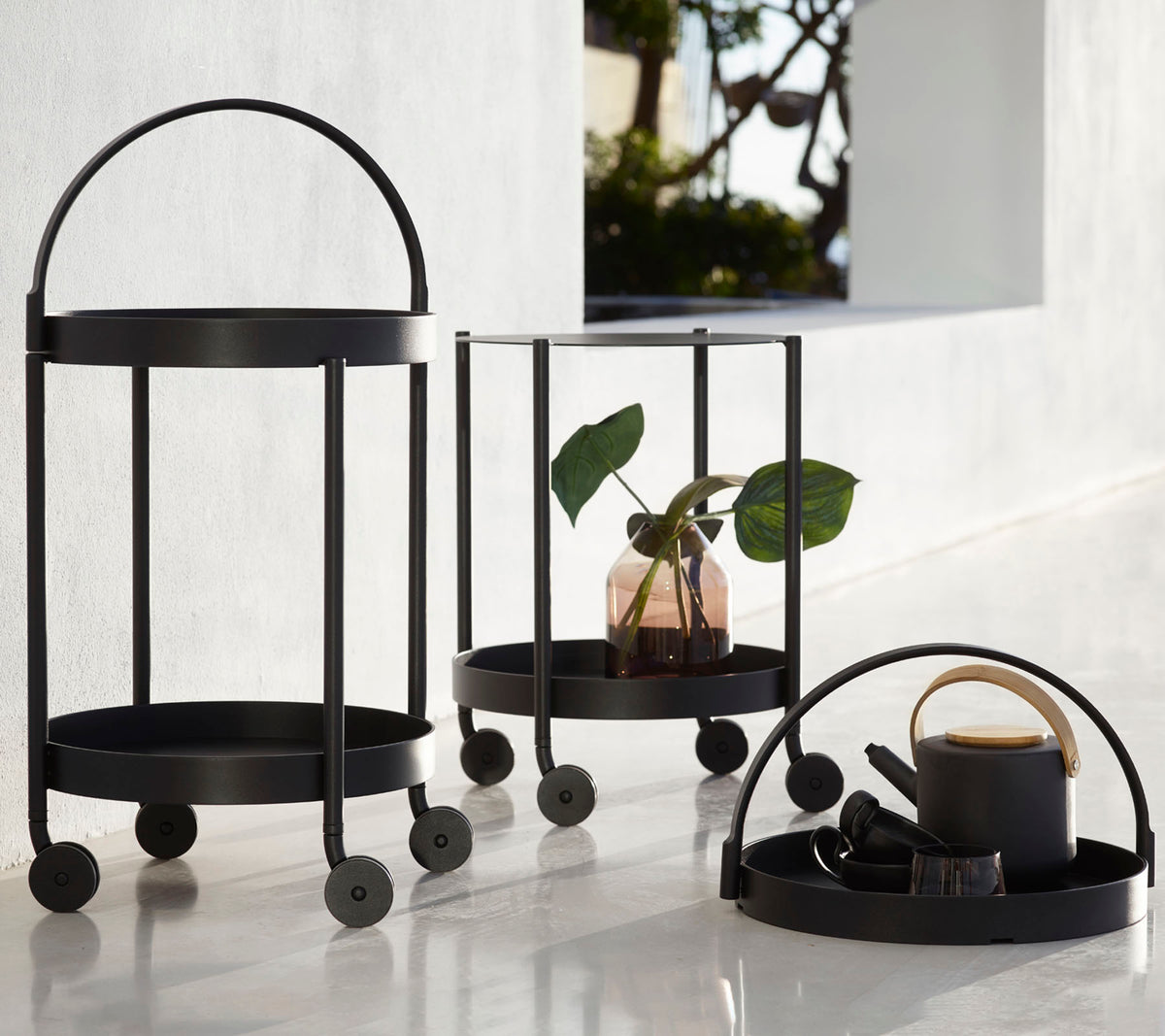 Three black metal carts with circular frames and wheels, featuring a plant, decorative items, and a cup, arranged for display.