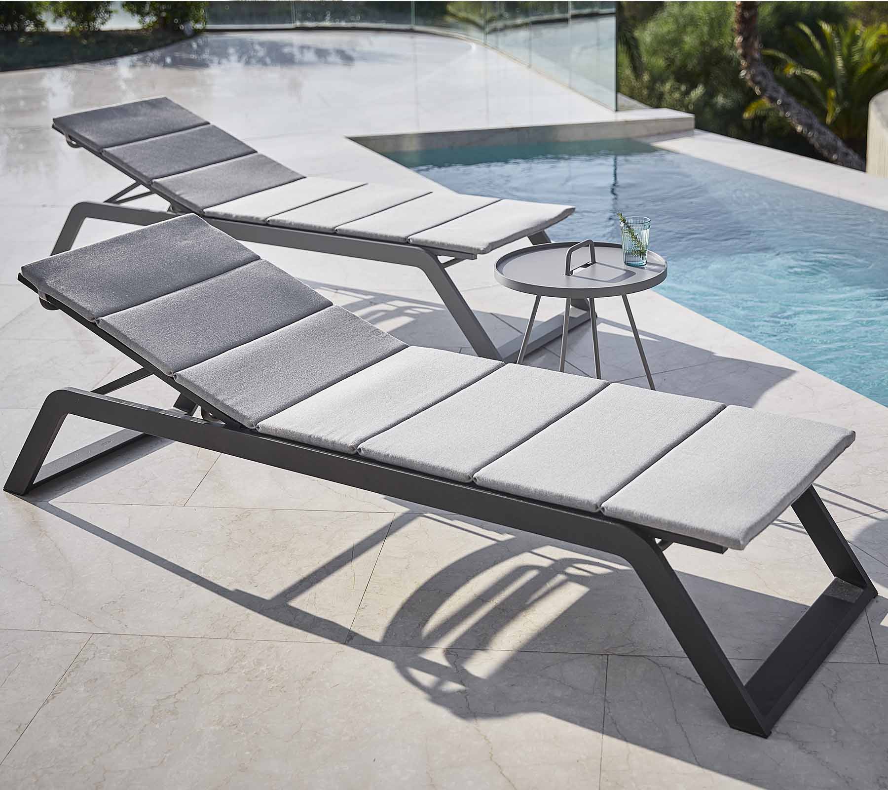 Two stylish lounge chairs with gray cushions are positioned beside a pool, accompanied by a small side table with a drink.