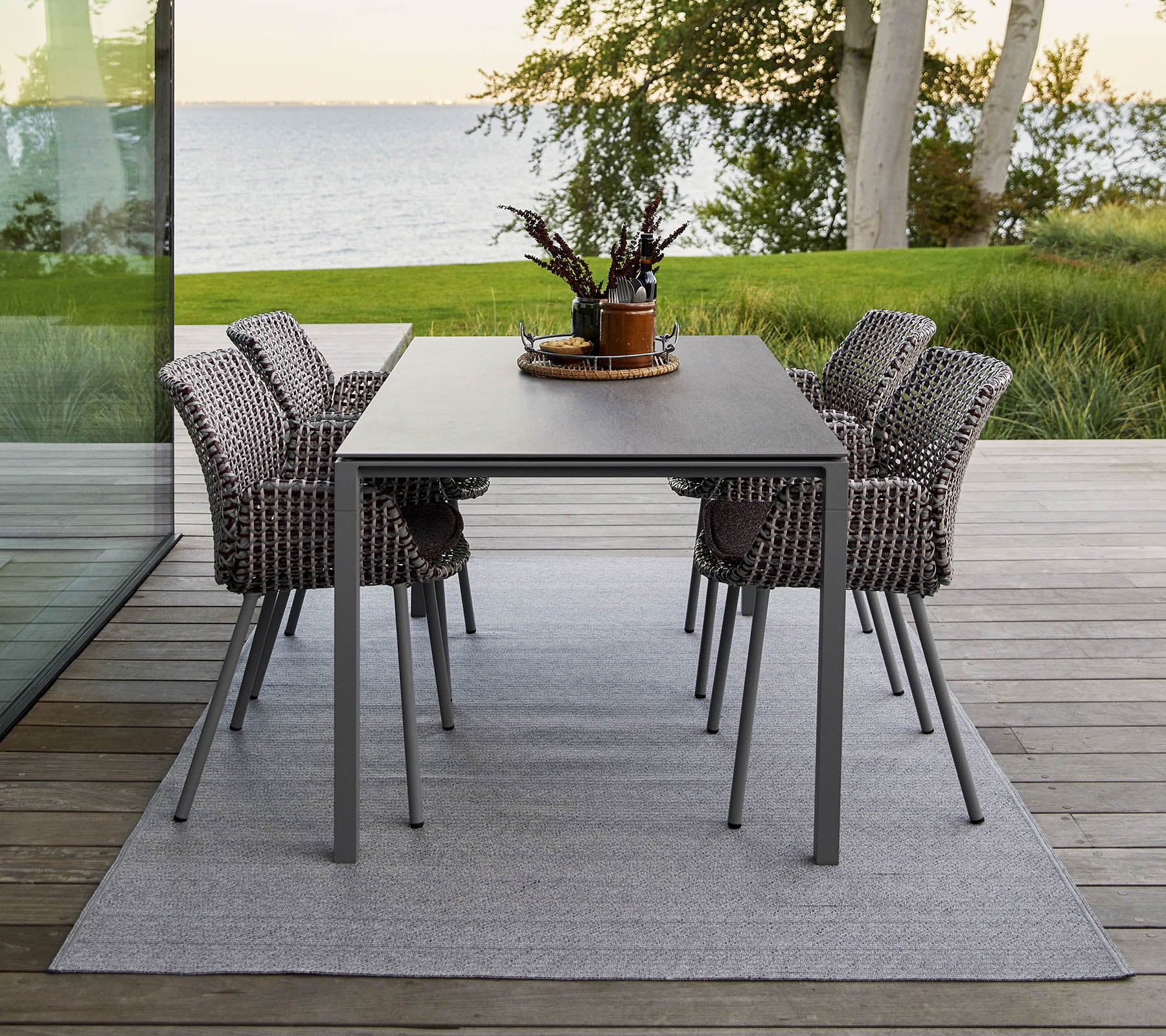 A modern dining table with four stylish woven chairs, adorned with a decorative plant centerpiece on a soft rug.