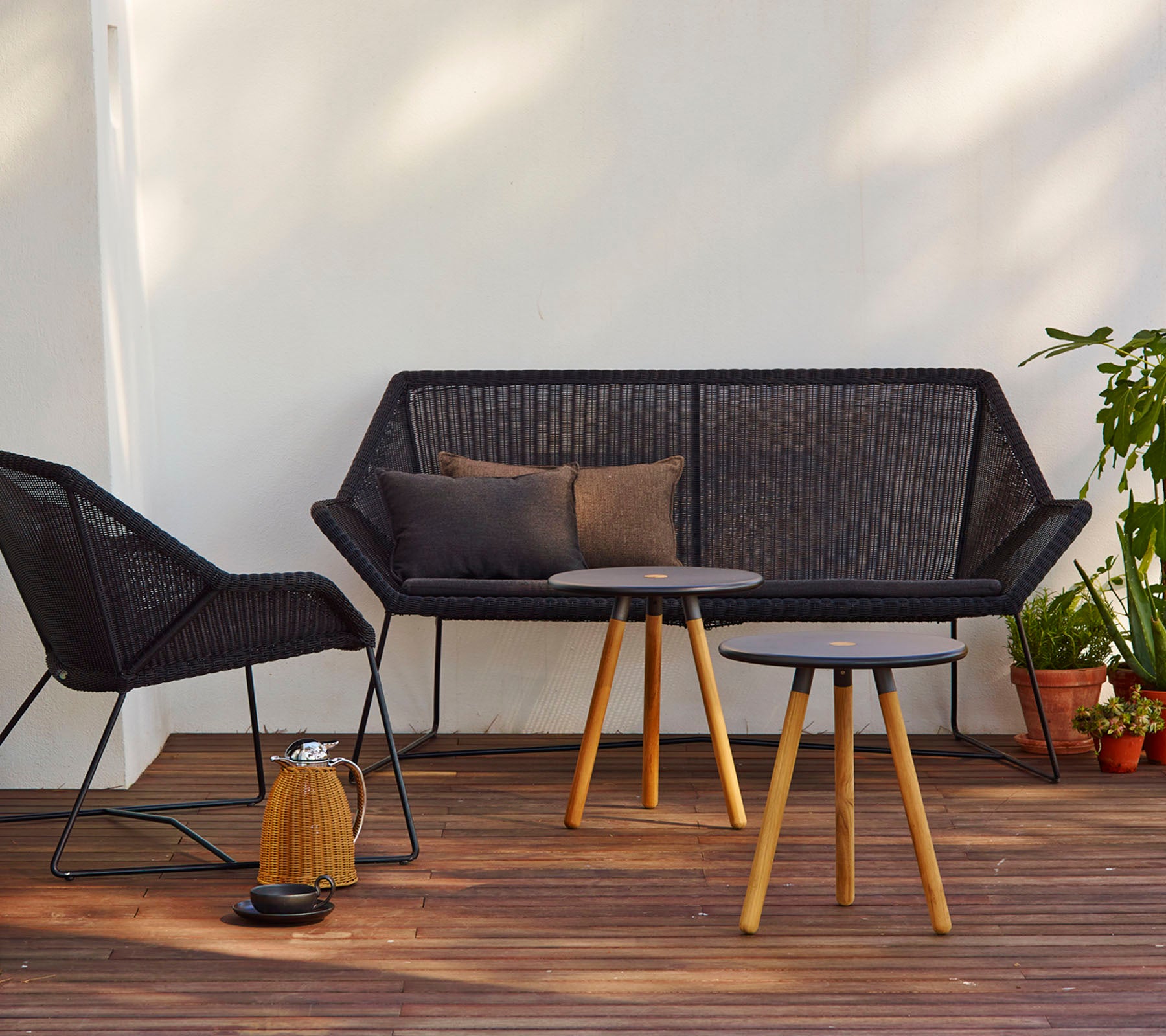 Contemporary seating arrangement featuring a black couch with cushions, a matching chair, and a round table with wooden legs.