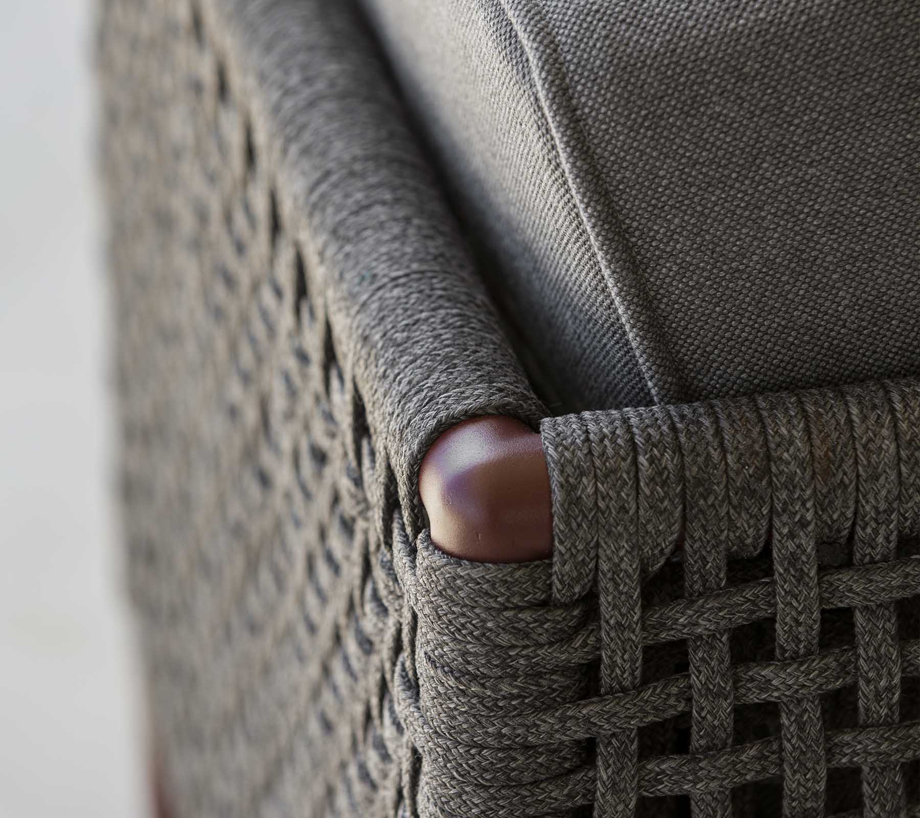 Close-up of a woven furniture corner featuring elegant gray fabric and smooth wooden accents, showcasing a blend of texture and style.