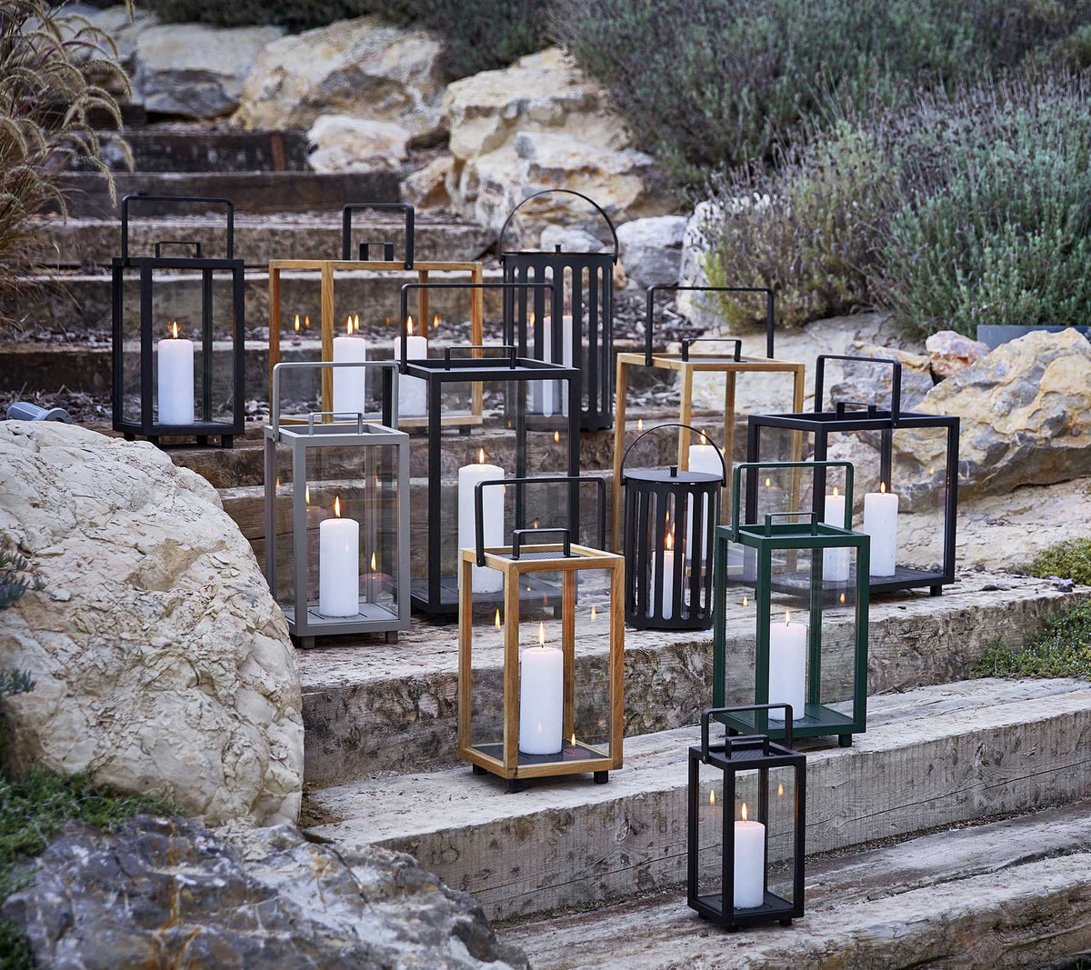 Collection of decorative lanterns in various styles and colors, featuring soft candlelight, arranged artistically on stone steps.
