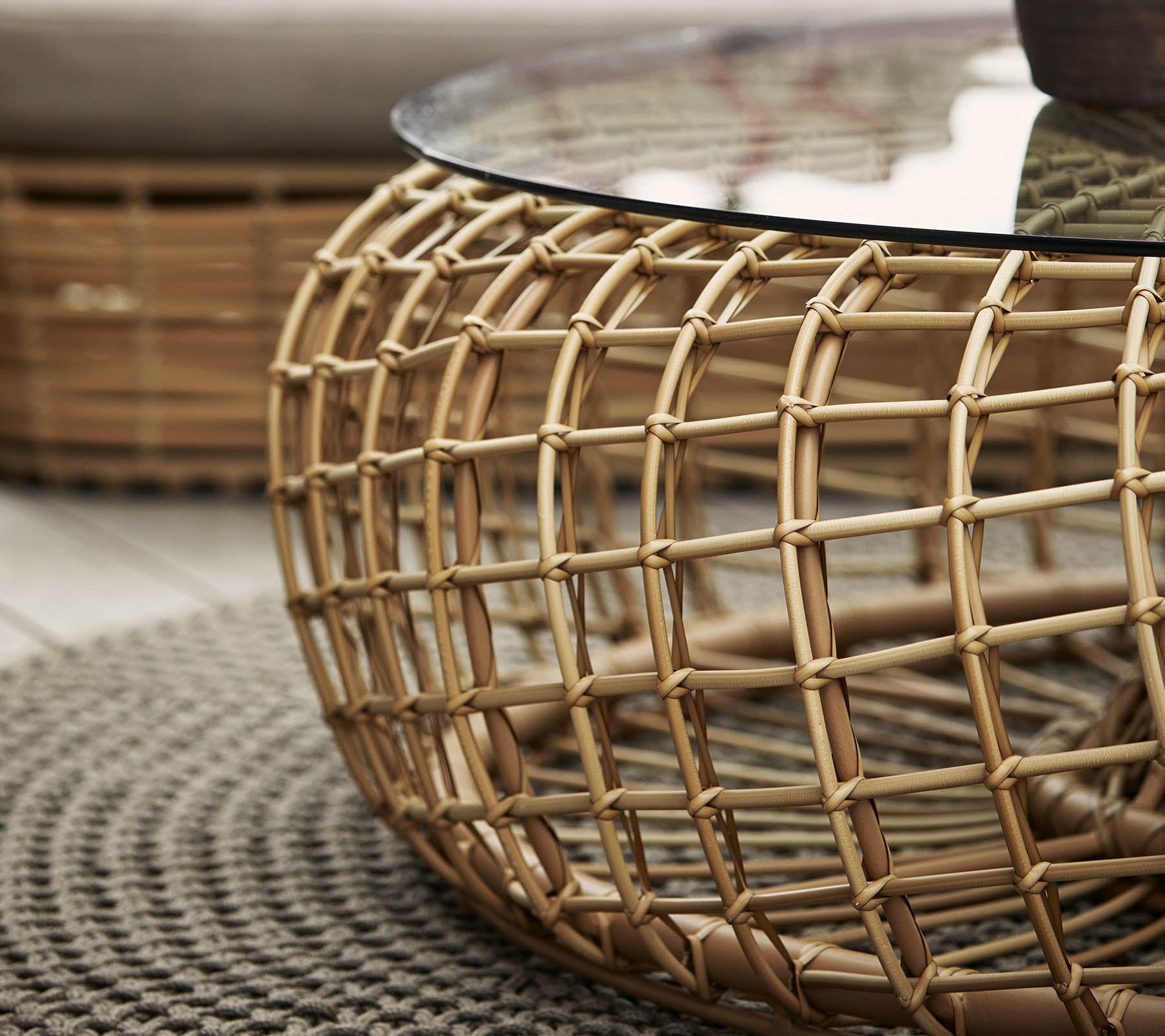 Round coffee table featuring a woven rattan base and a glass top, complemented by a textured circular rug.