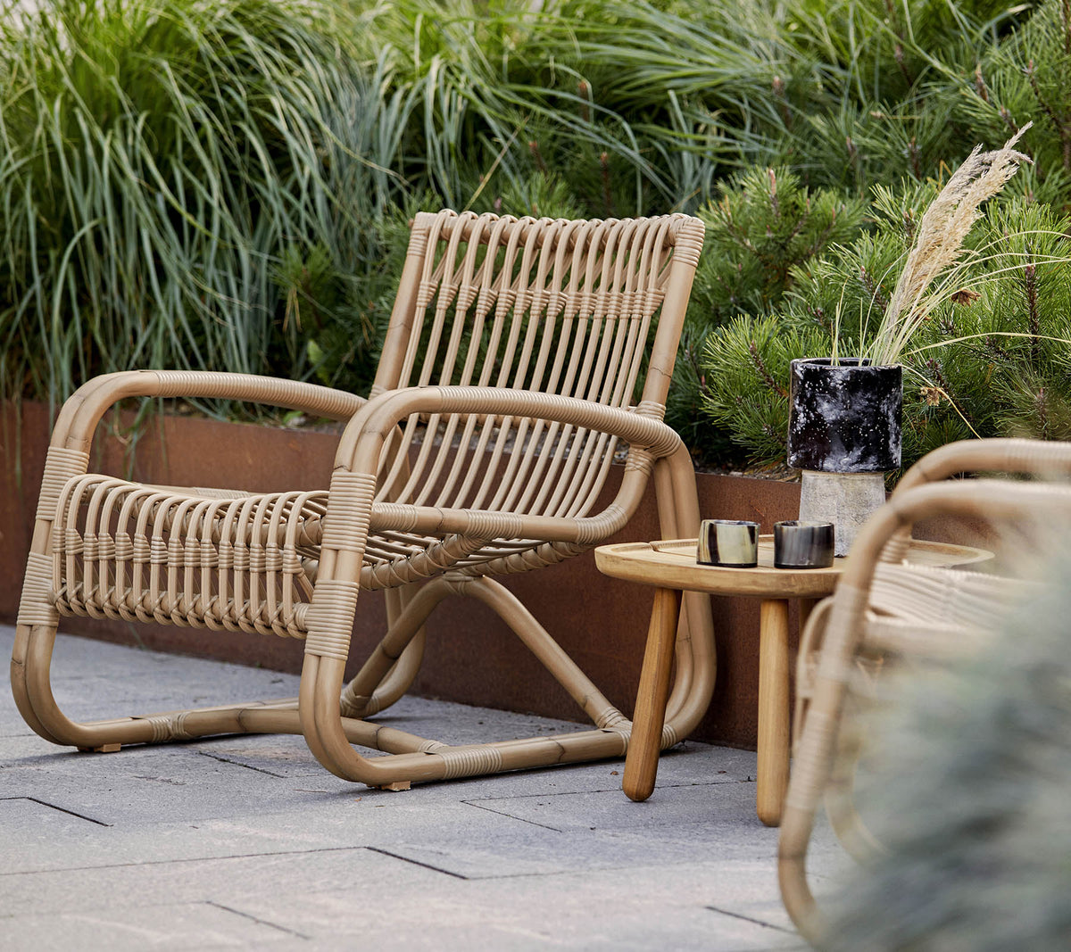 A natural woven chair accompanied by a small wooden table and decorative elements, surrounded by lush greenery.