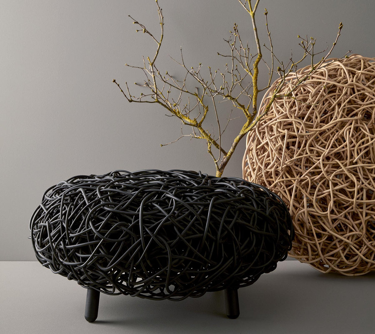A stylish, round coffee table made of woven material, showcasing black and natural tones, with a decorative branch placed on top.