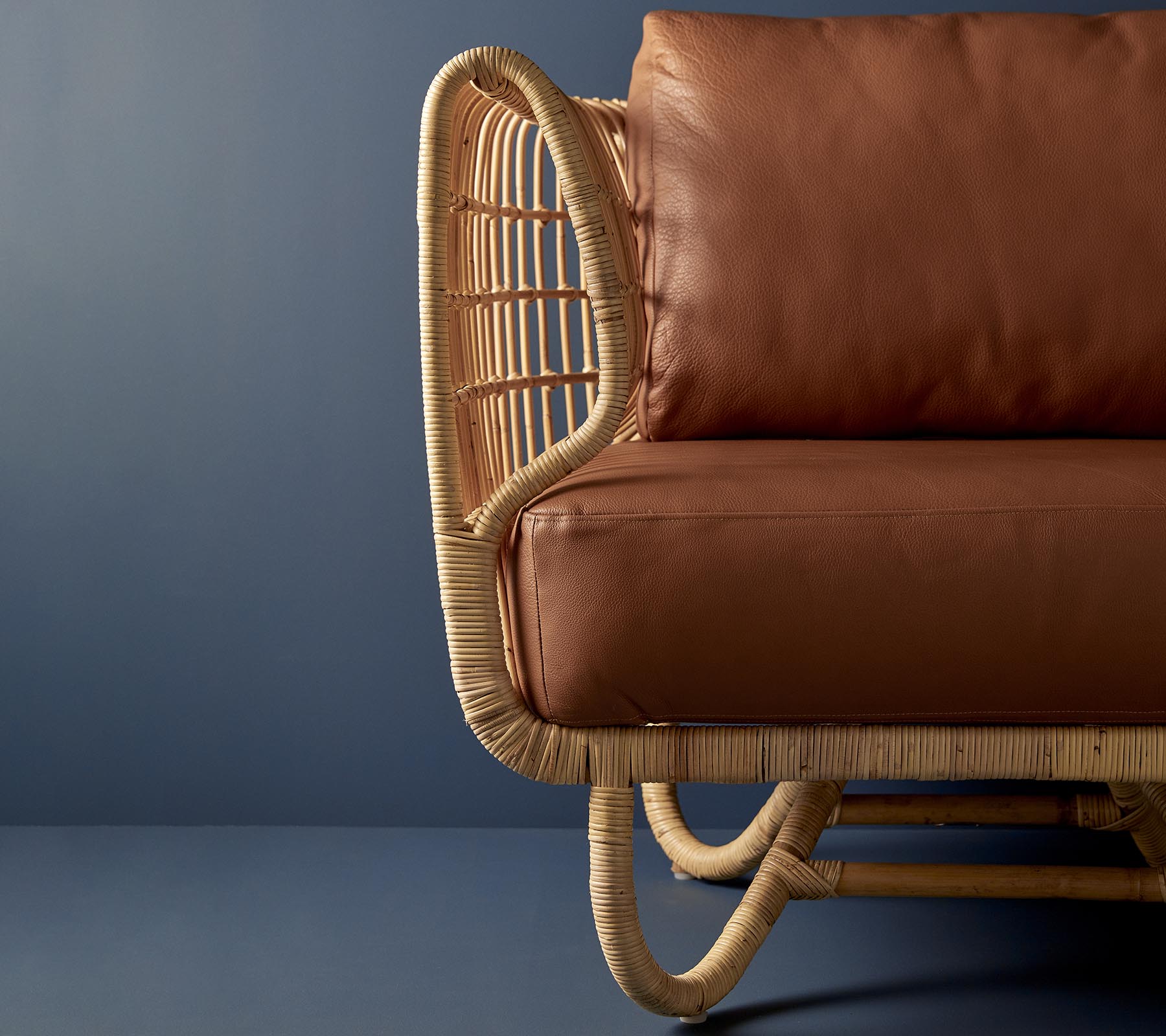 Rattan chair with a curved design and brown leather cushions, showcasing a blend of natural materials and modern aesthetics.
