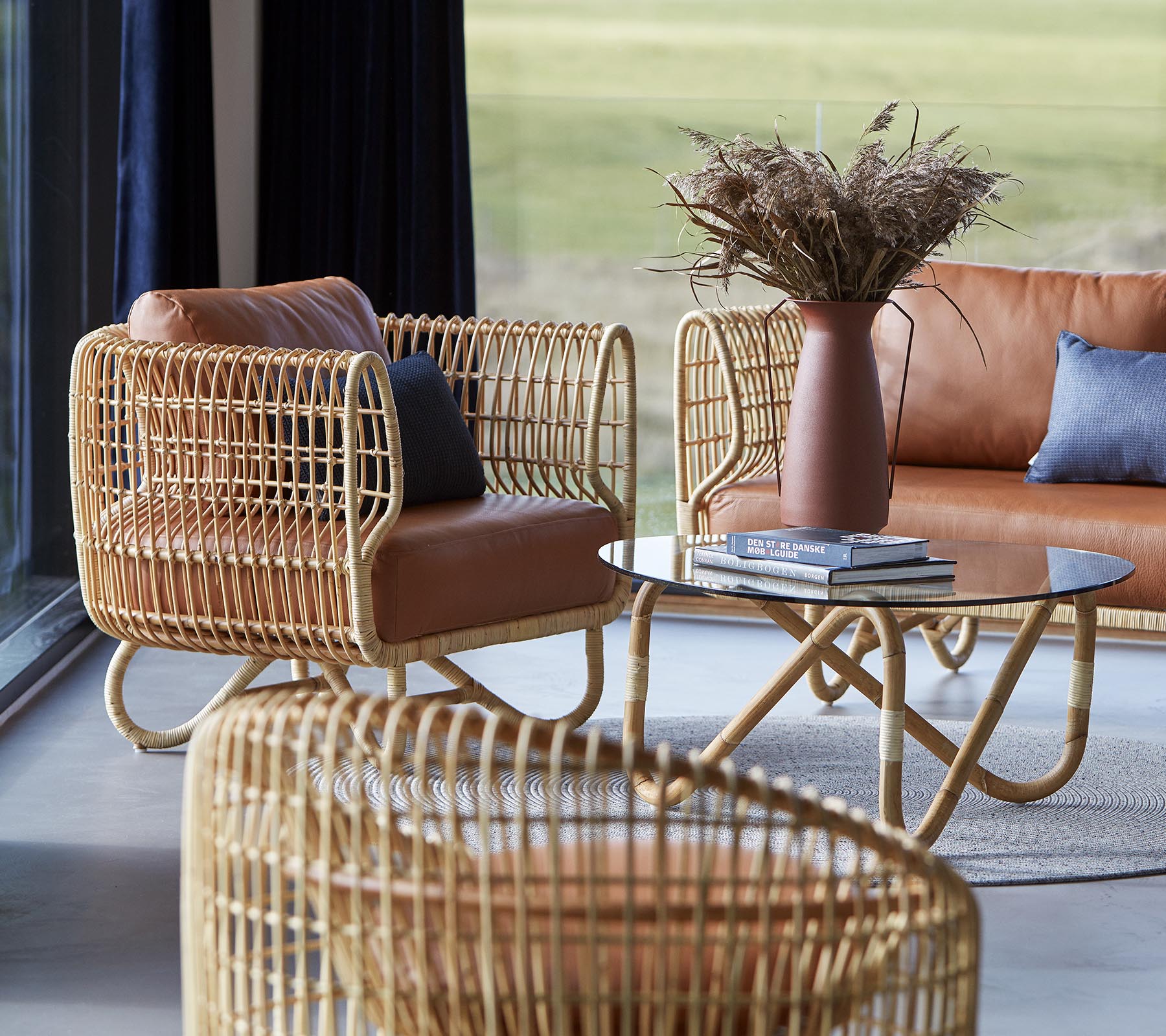 Stylish seating with woven rattan frames, leather cushions, a sleek coffee table, and a vase with dried foliage, creating a cozy atmosphere.