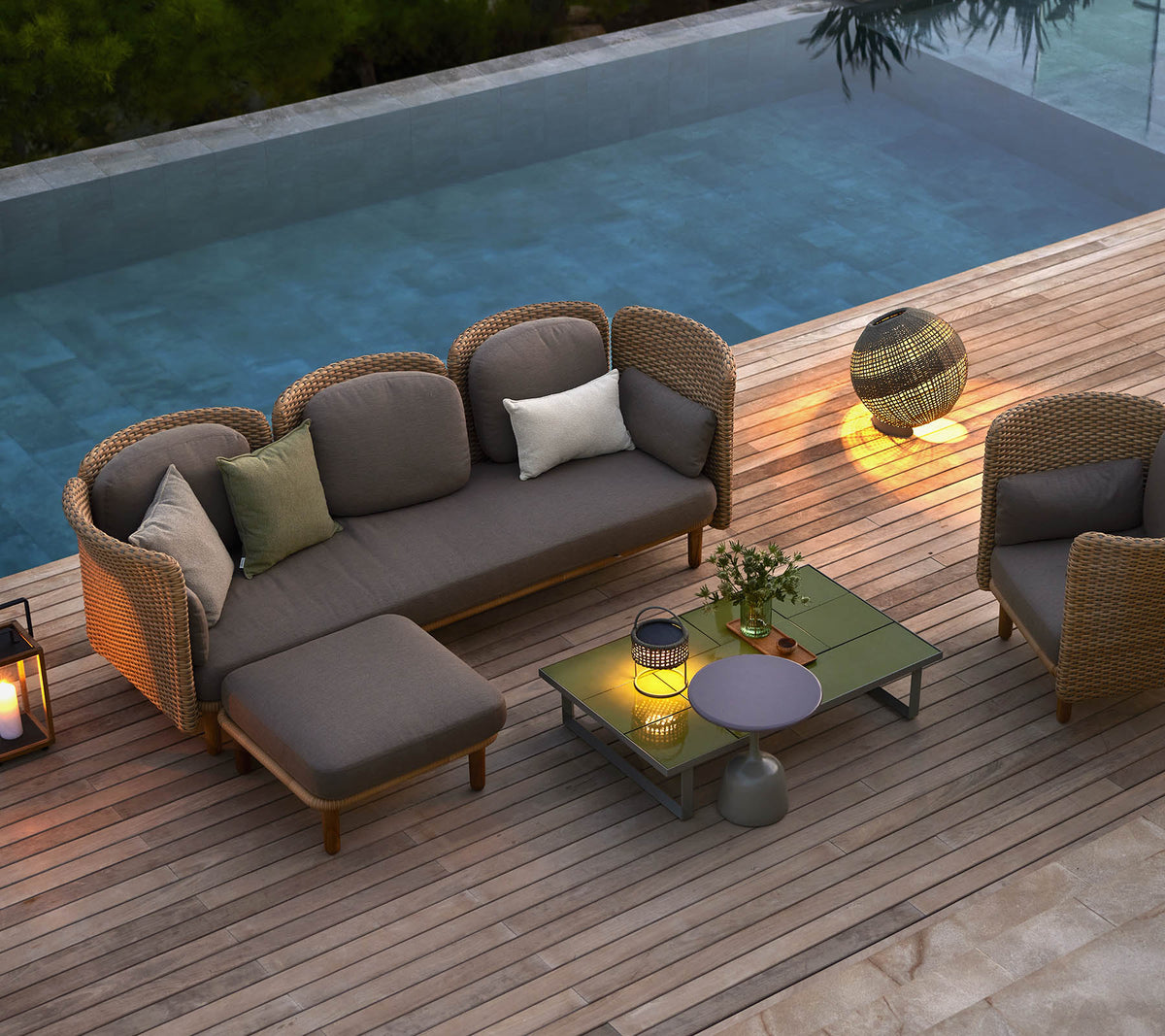 Stylish lounge seating with cushions, a coffee table, and ambient lighting, set beside a serene pool.