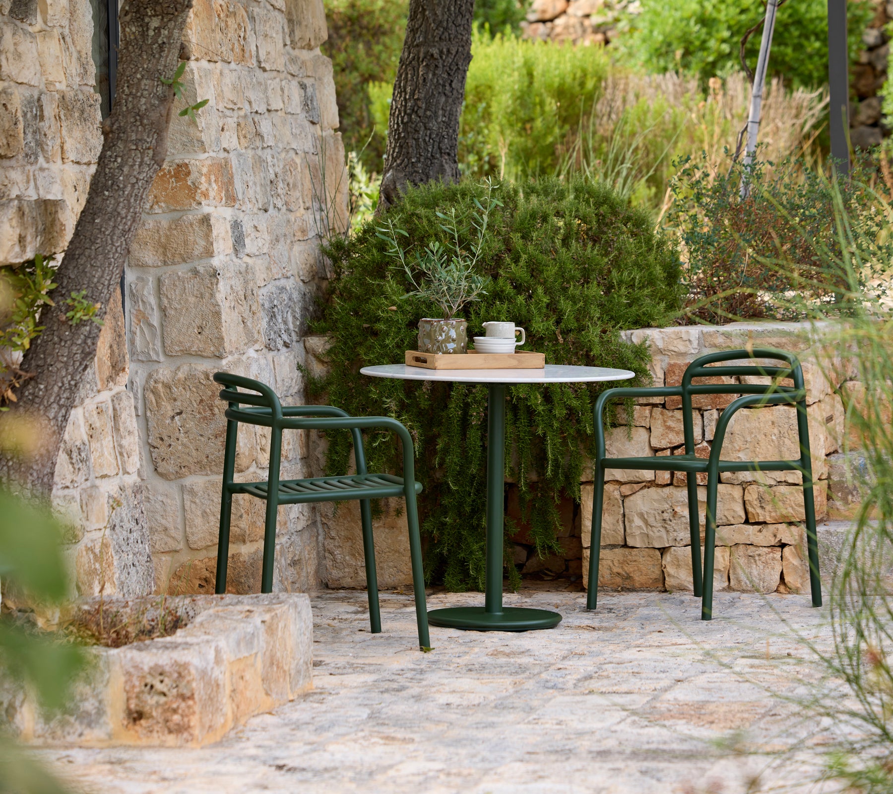 Green chairs surrounding a round table in an outdoor stone setting.