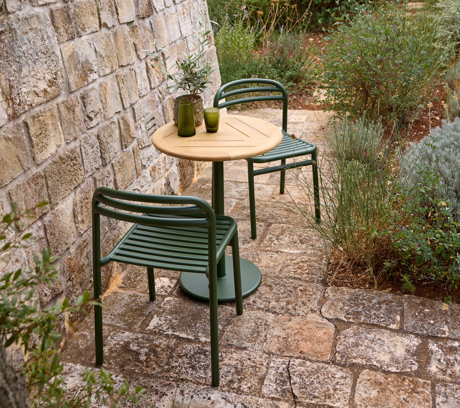 Outdoor setting with a green chair, wooden table, and glass vase.