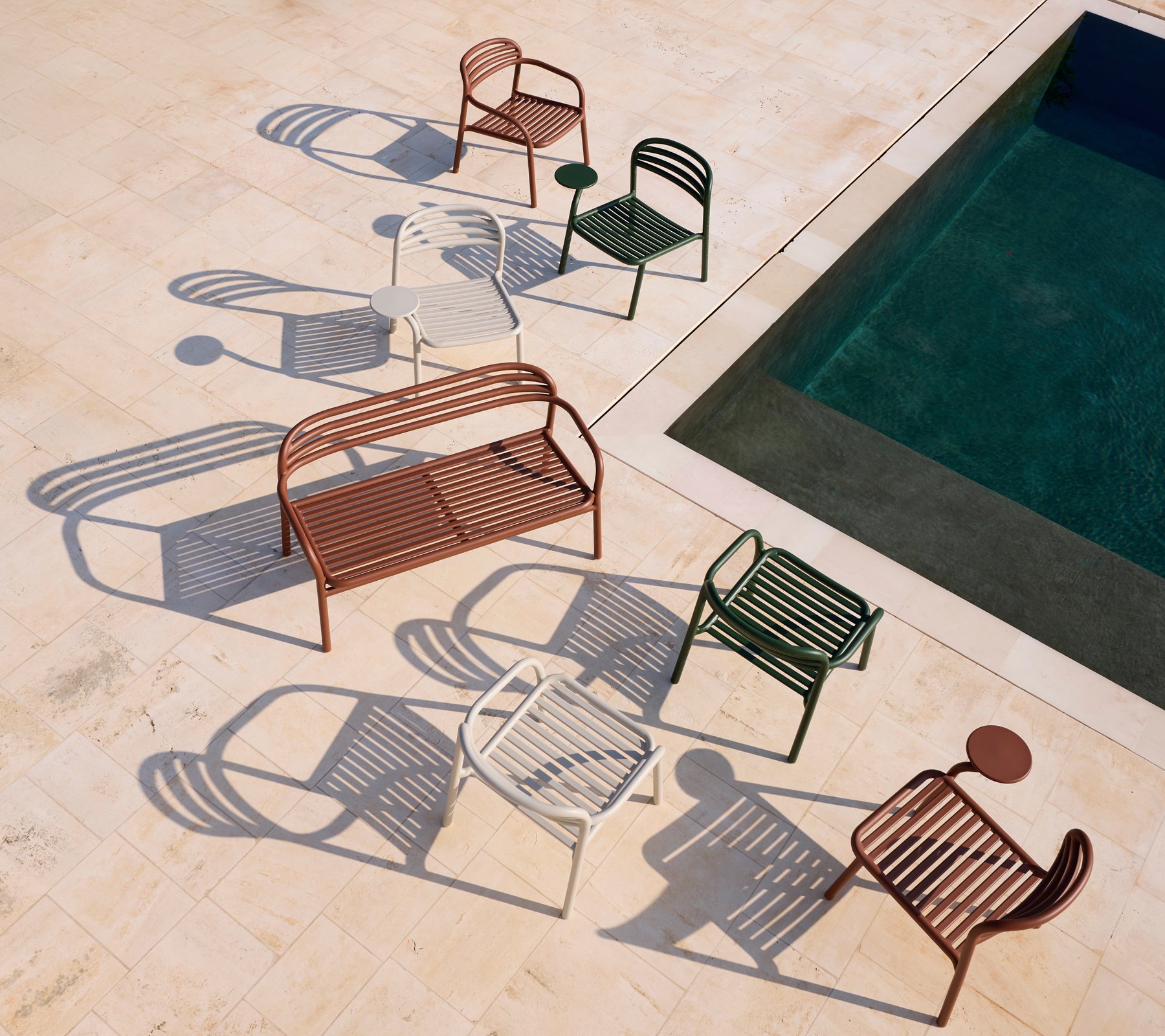 Set of modern red, white, green chairs and a brown bench near a pool.