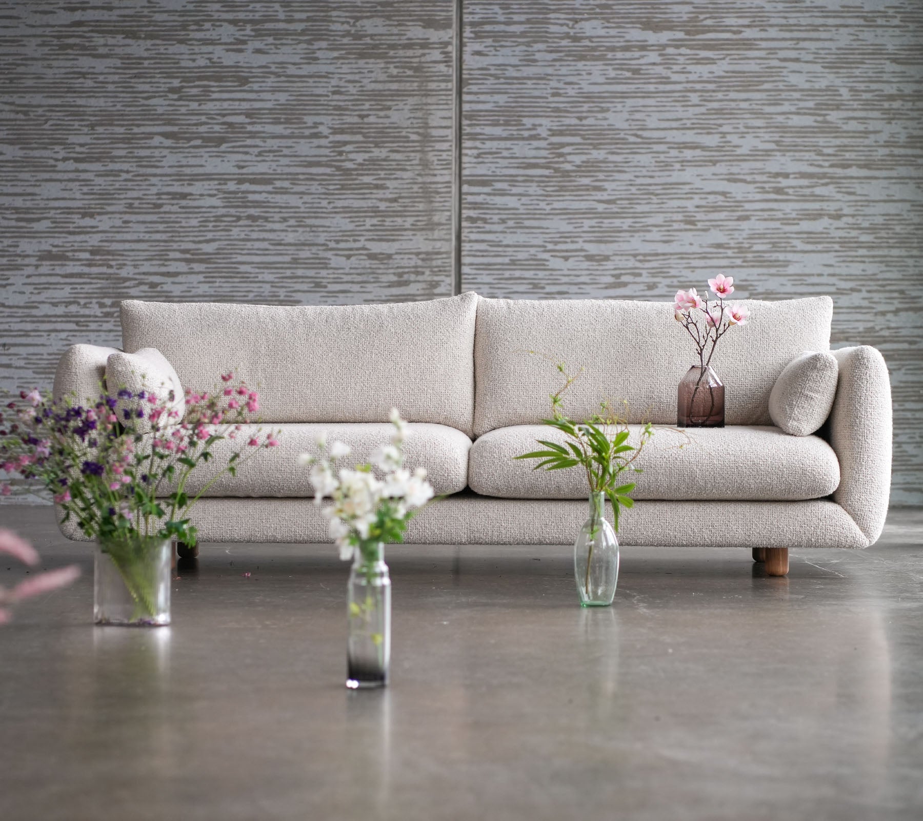 A light-colored sofa with teak legs, surrounded by vases of flowers, showcasing a blend of elegance and Cane-line flair.