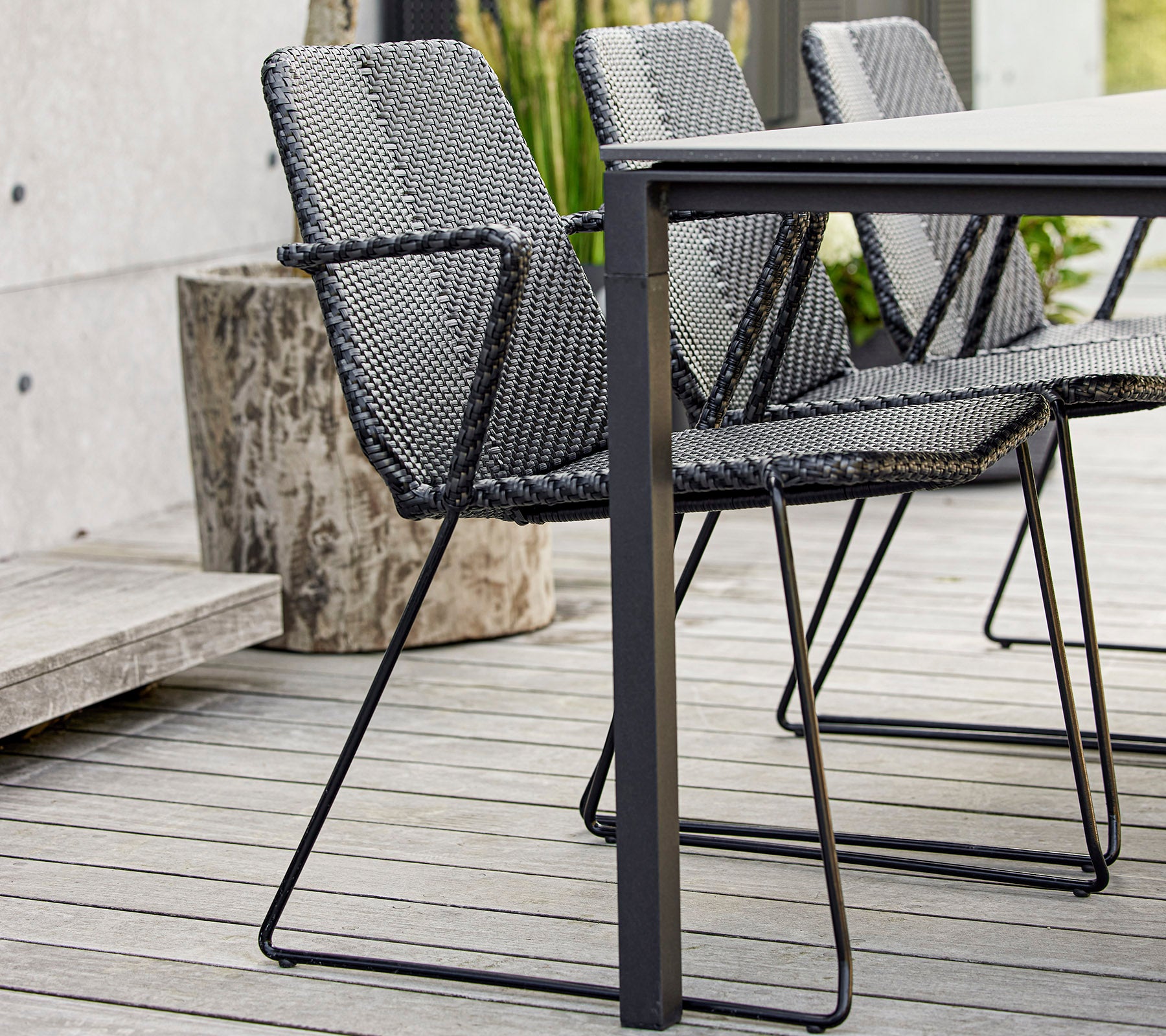 A set of modern black woven chairs positioned around a sleek table, showcasing contemporary design and craftsmanship.