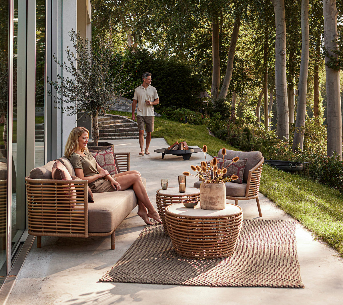A stylish outdoor seating area featuring woven furniture, a decorative coffee table, and a relaxed atmosphere with greenery in the background.