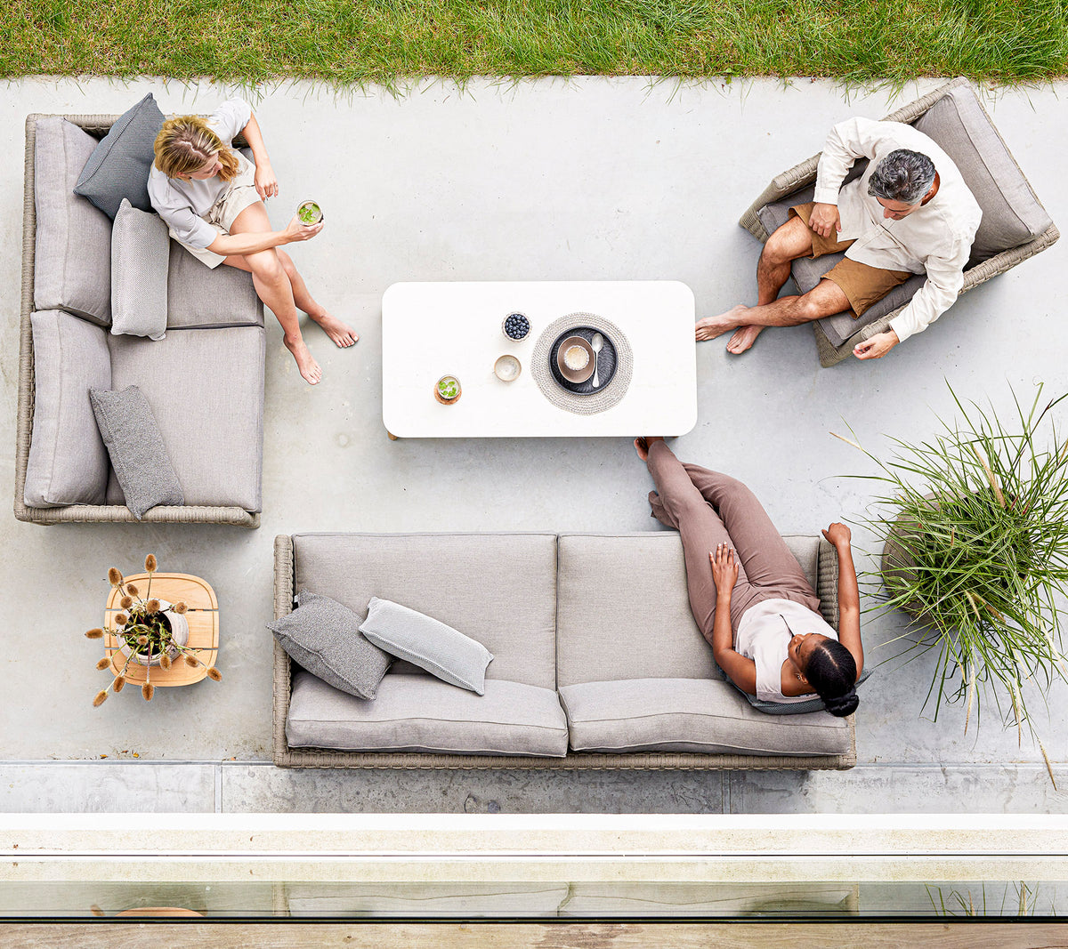 Three people relax on stylish light gray seating around a minimalist coffee table, enjoying drinks and conversation in a serene setting.