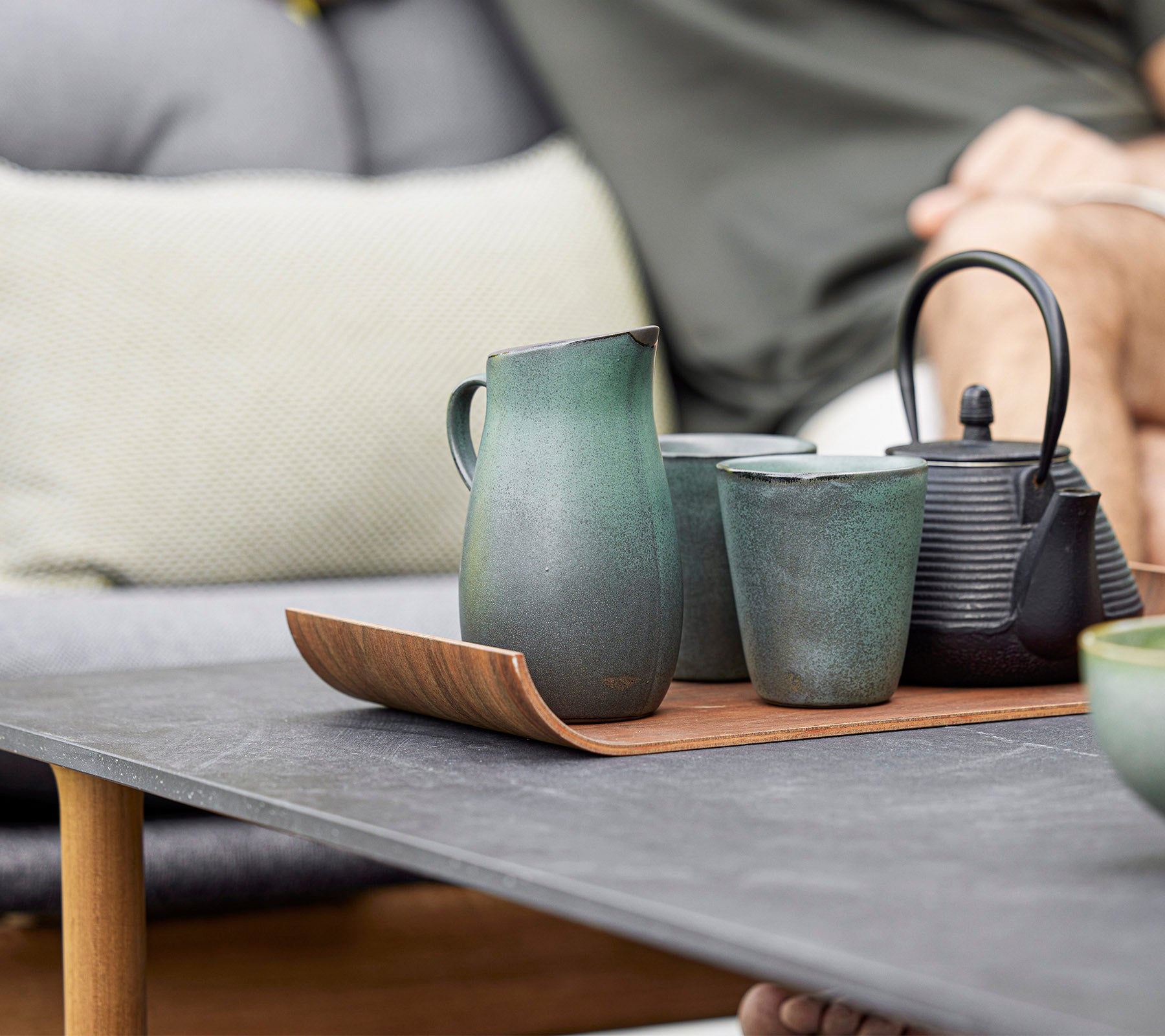 A stylish arrangement of ceramic teapot, cups, and a pitcher on a wooden tray, showcasing modern design and earthy tones.