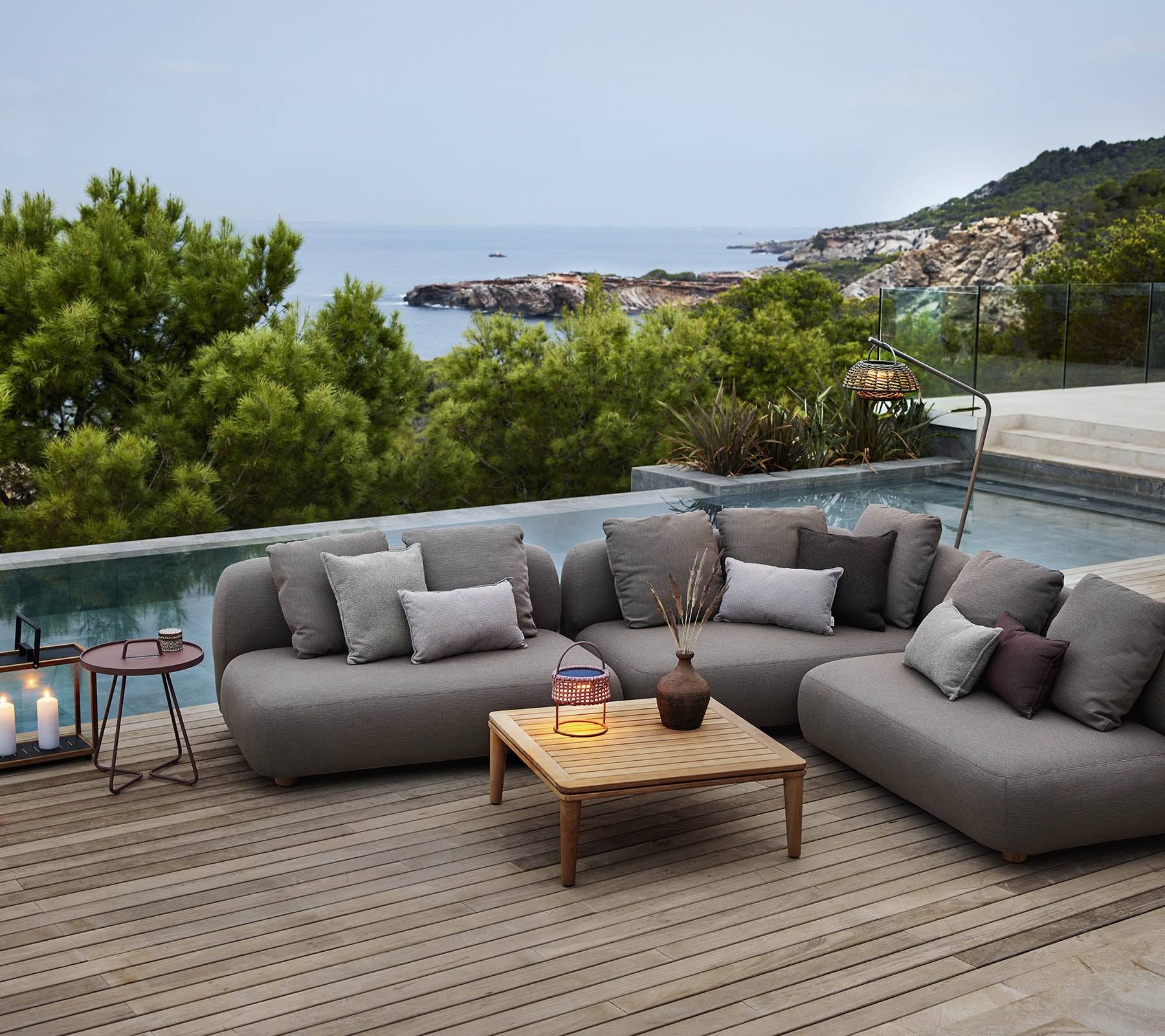 Stylish lounge seating with cushions, a wooden coffee table, and decorative candles, set against a serene ocean backdrop.