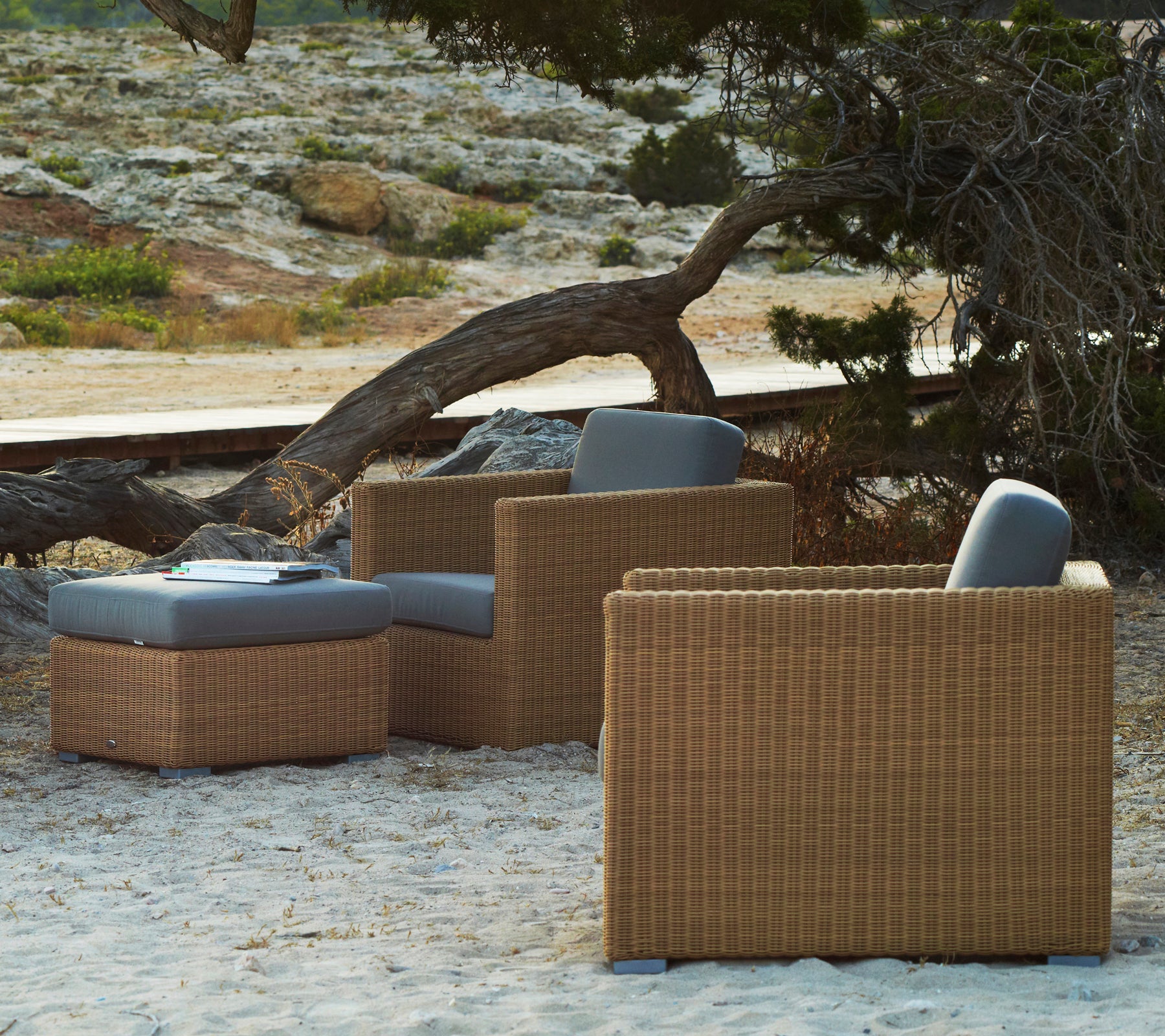 Rattan lounge chairs with grey cushions in a natural outdoor setting.