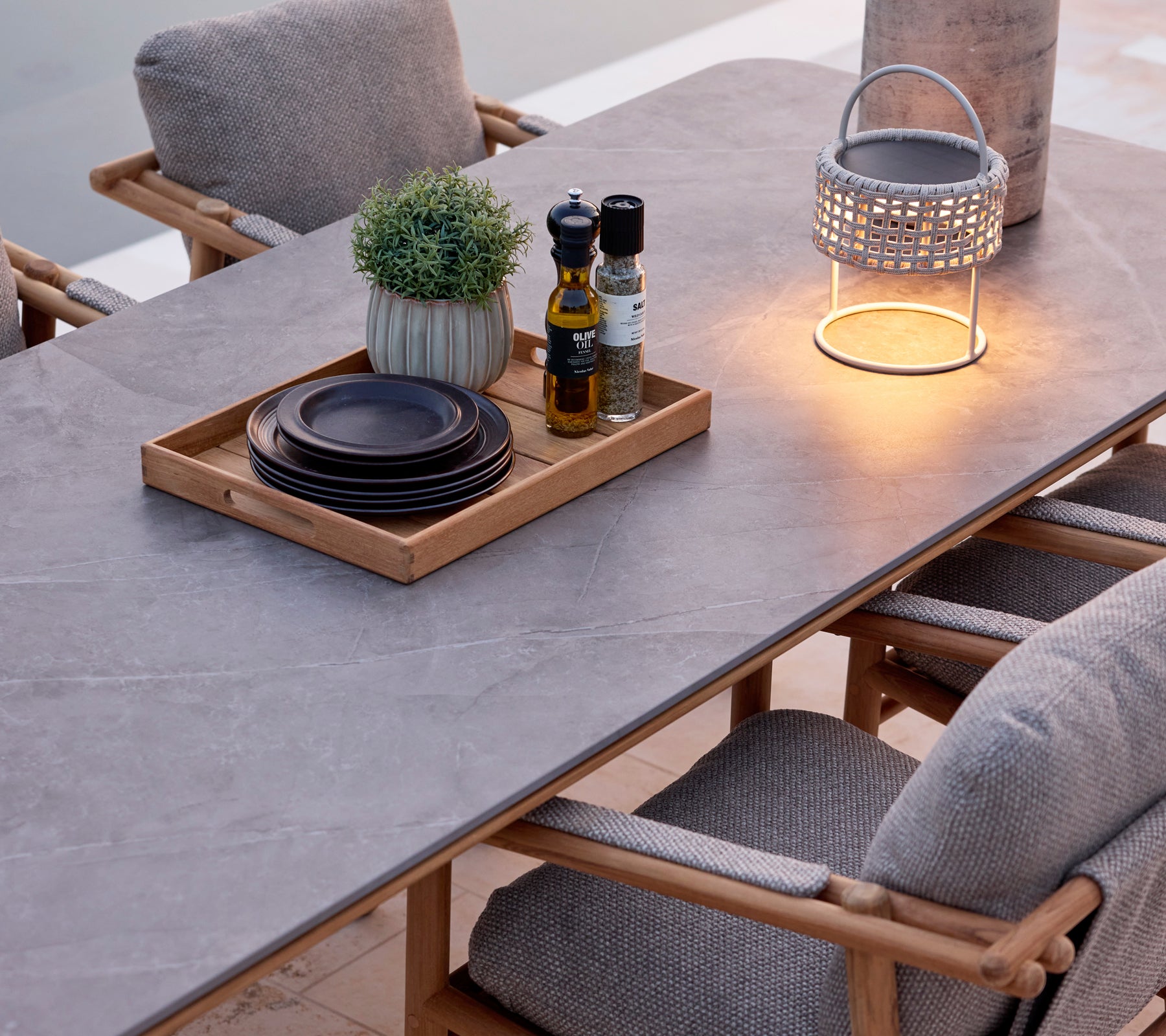 Modern dining table with grey surface, brown chairs, black plates, and a decorative lantern.