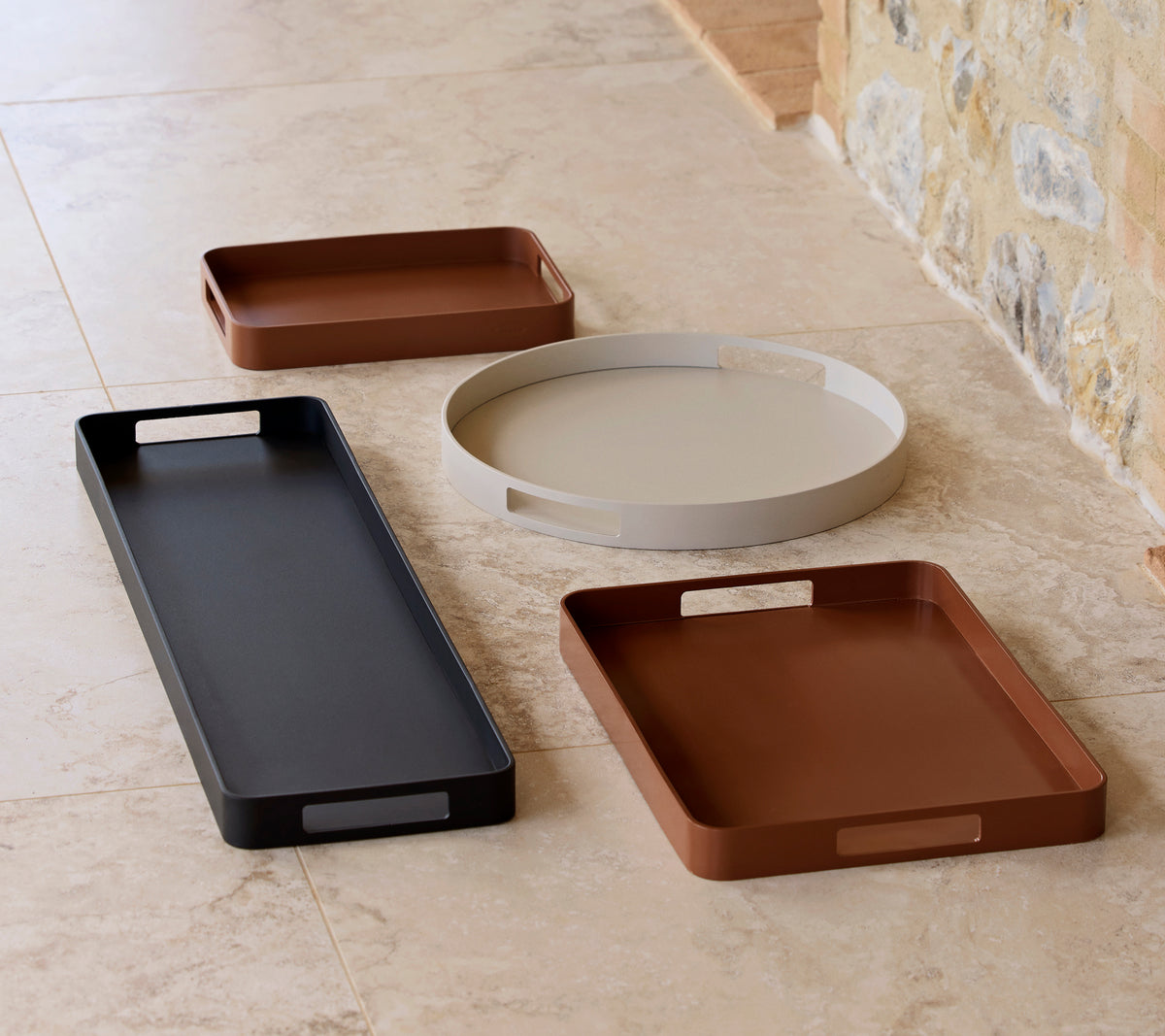 Four stylish club trays in various shapes and colors, including black, brown, and light gray, arranged on a neutral surface.