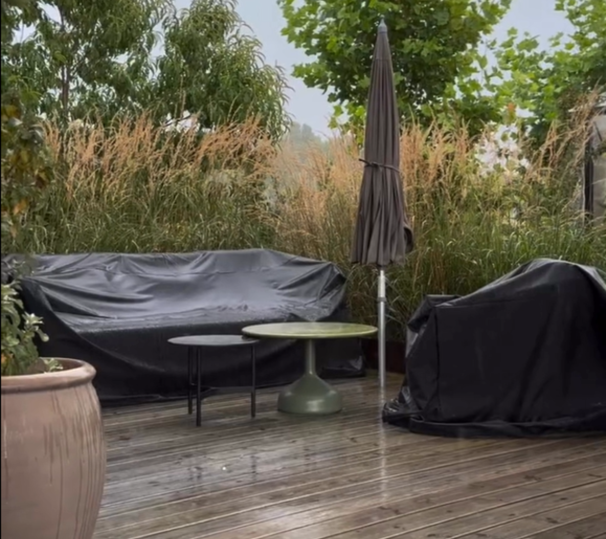 Outdoor space with black sofa, green table, and black chair surrounded by greenery.