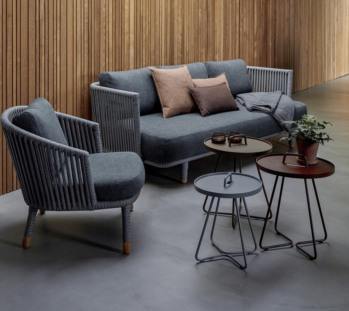 Stylish seating arrangement featuring a grey sofa with cushions and two accent chairs, accompanied by three modern tables and a potted plant.