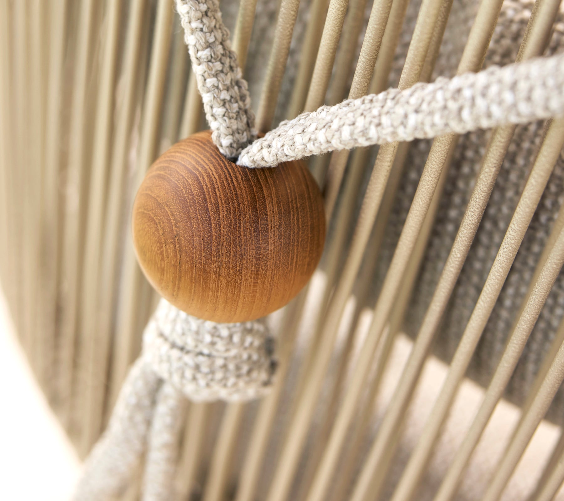Close-up of a neck cushion holder for a Hive chair, featuring a wooden bead and woven fabric straps.