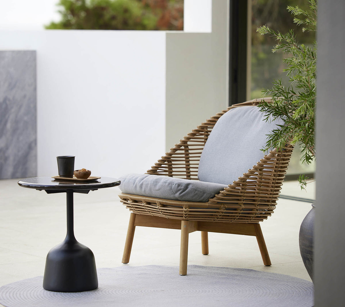 A stylish lounge chair with a woven design and soft cushions, accompanied by a sleek side table and a small plant. Ideal for relaxation.