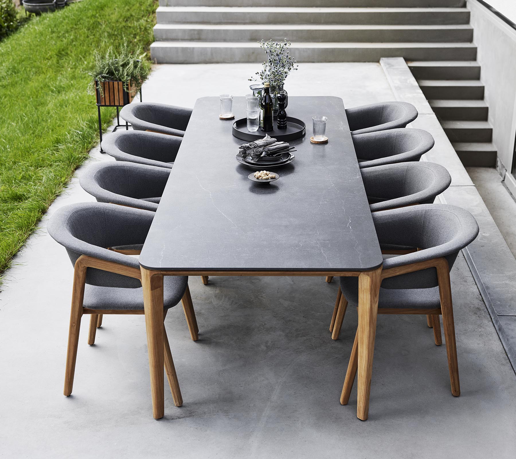 Stylish dining setup featuring a long table surrounded by modern upholstered chairs, adorned with decorative items and greenery.