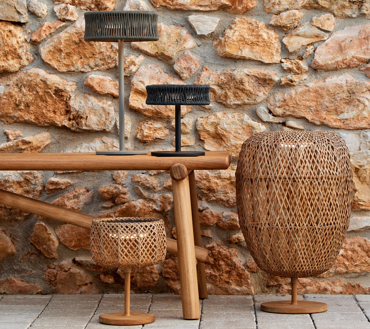 Three decorative lamps in varied shapes and sizes on a wooden table, set against a textured stone wall.