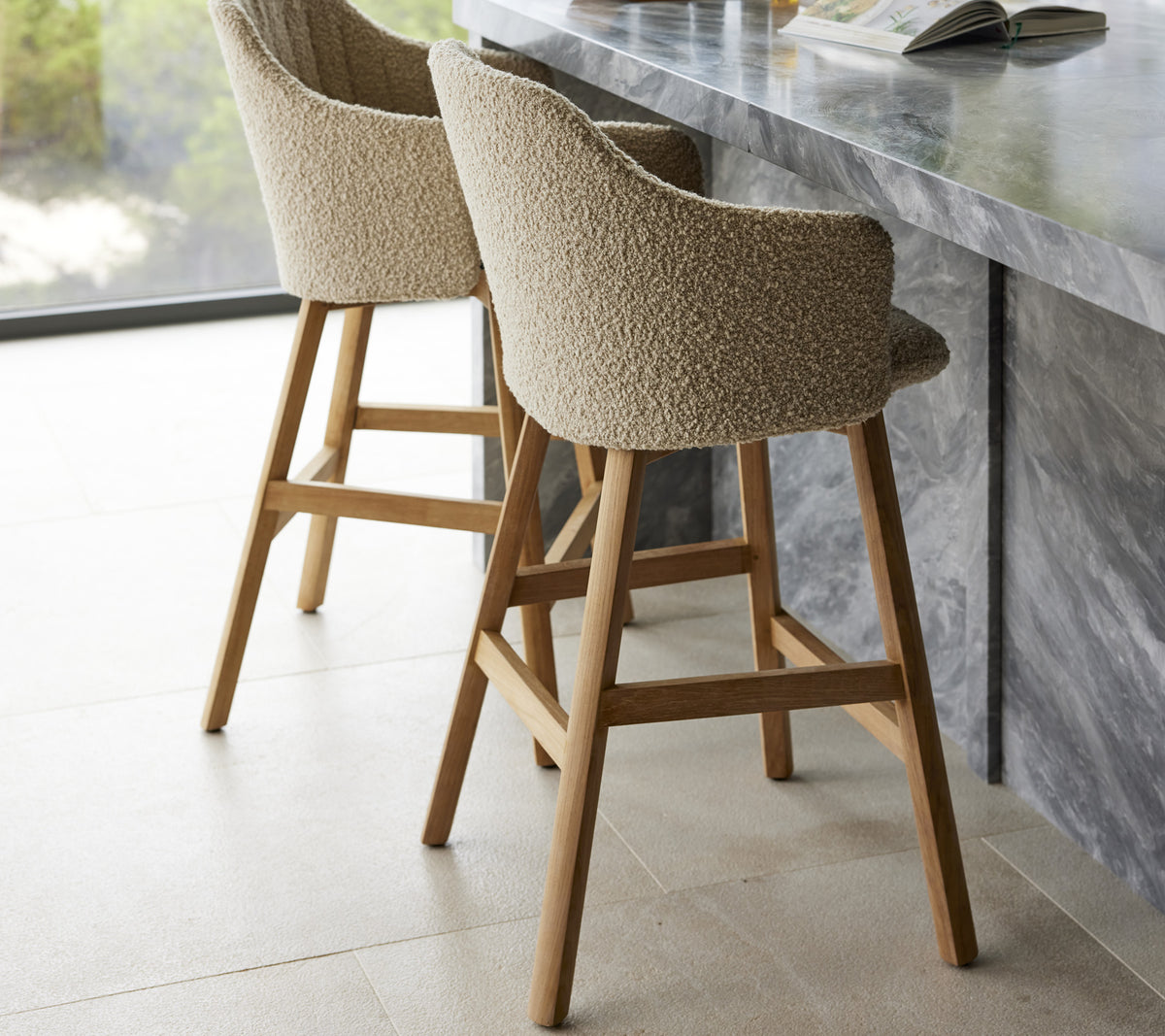 Two modern bar stools with cushioned seats and wooden legs positioned near a sleek marble counter.