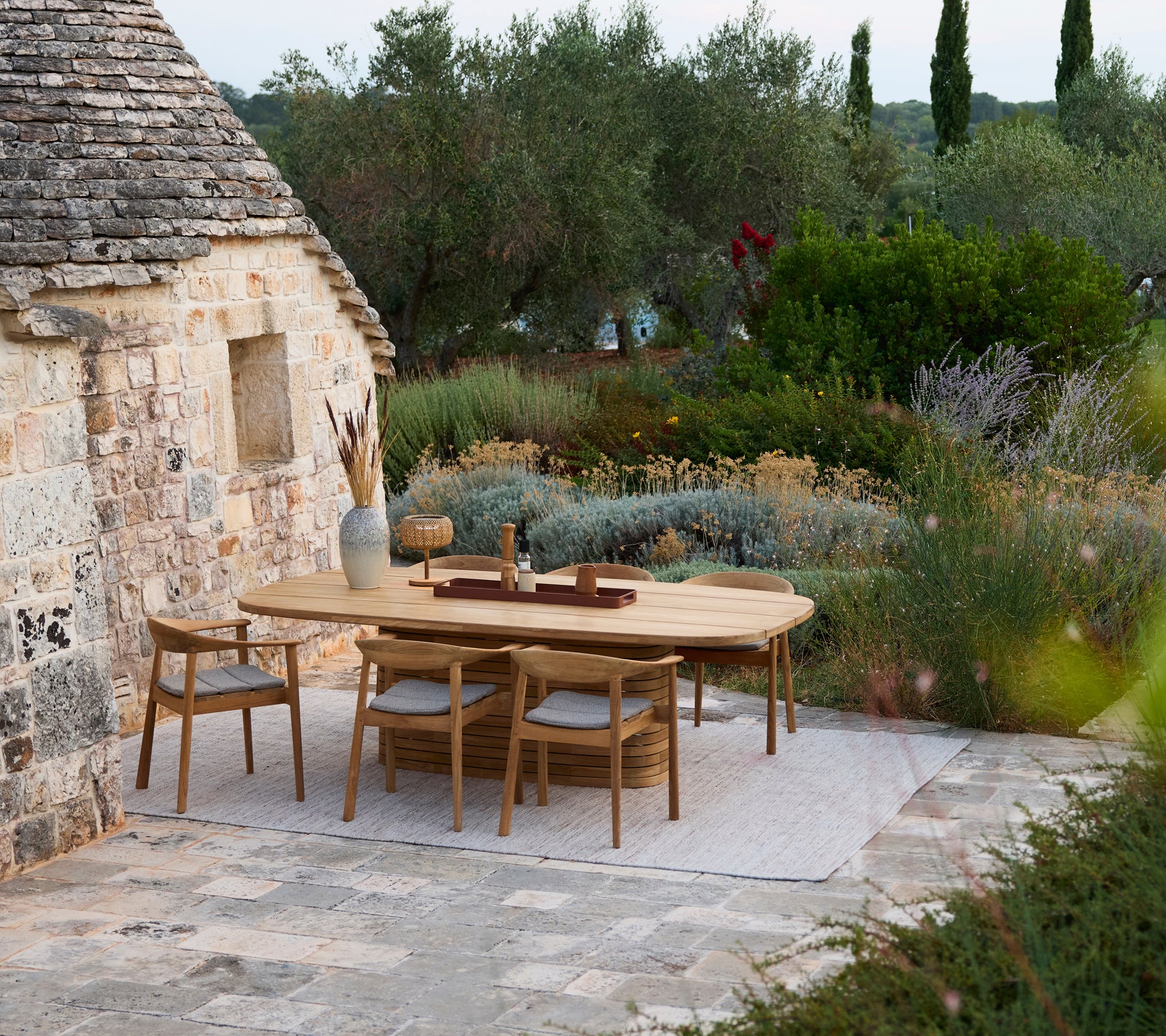 Modern wooden dining table surrounded by wooden chairs in an outdoor garden setting.