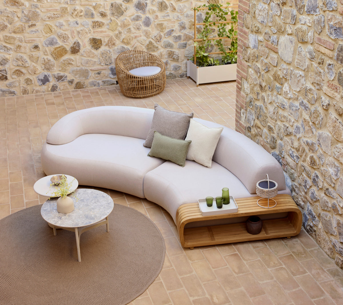 Curved mellow sofa with decorative cushions, a mellow coffee table, and a round nest chair, set on a textured floor.
