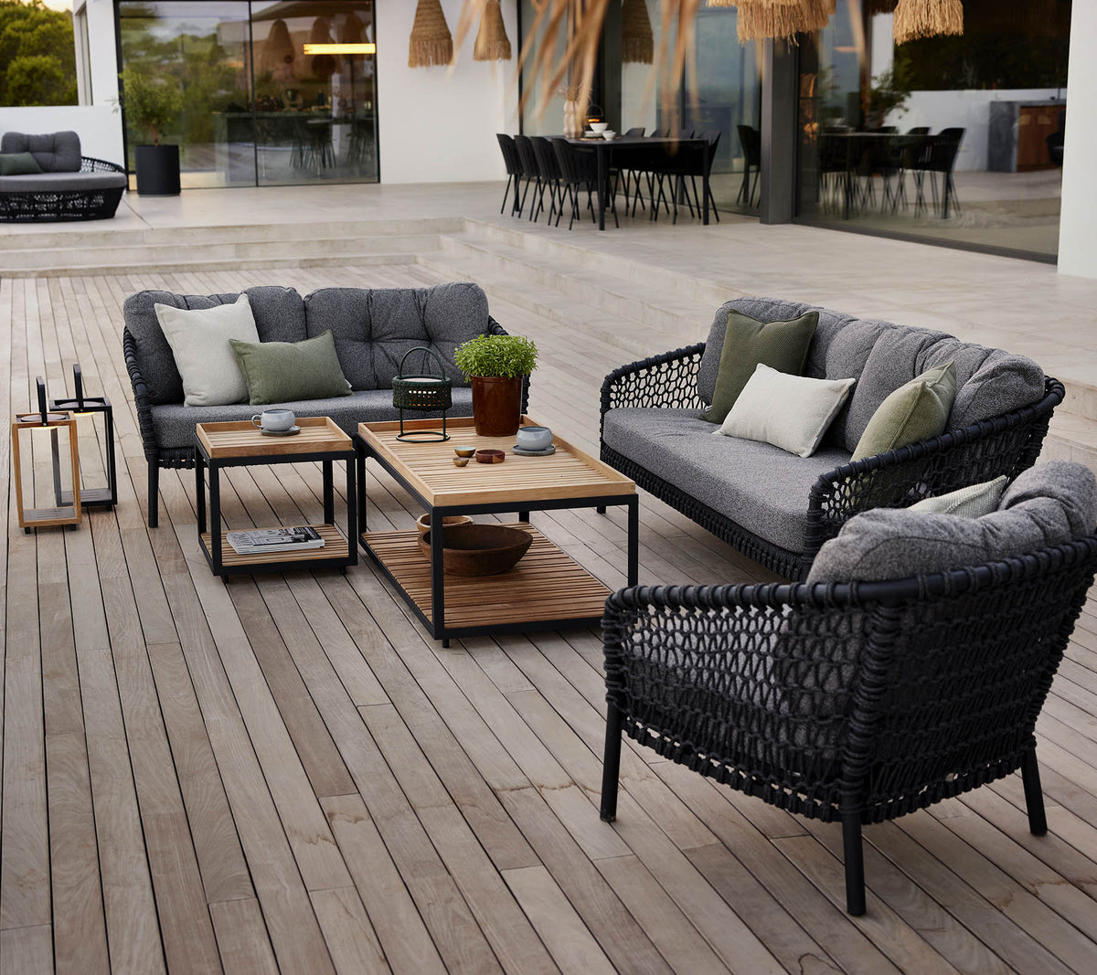 Stylish outdoor lounge area with black wicker furniture, gray cushions, a wooden coffee table, and potted plants on a wooden deck.