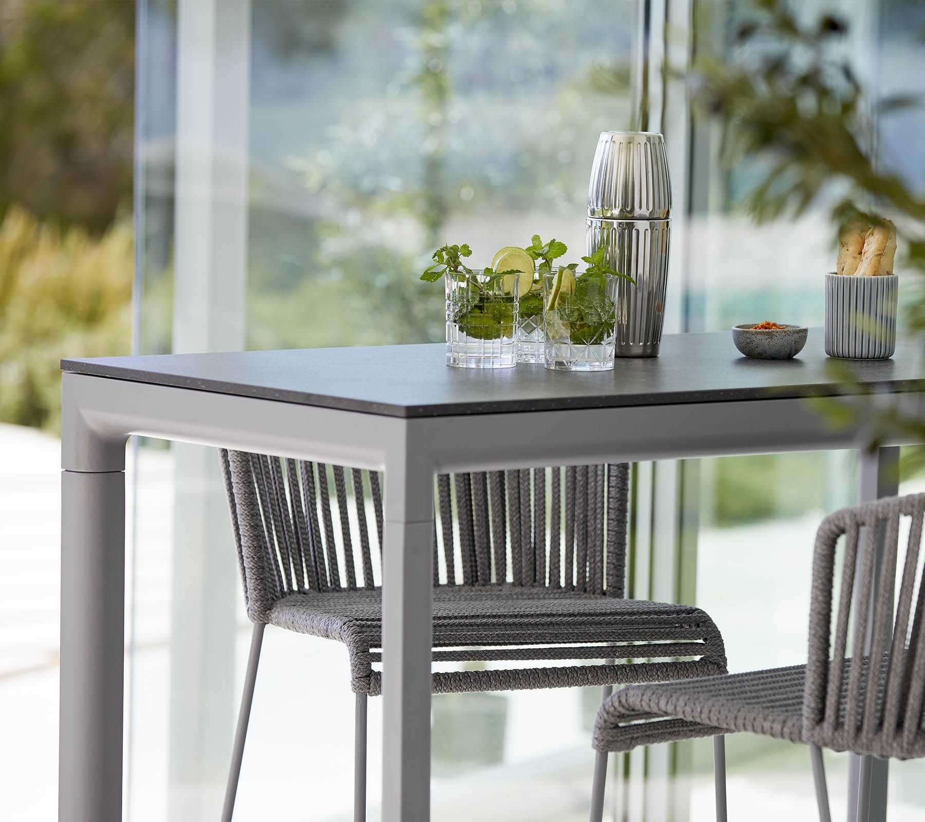 A modern table with two stylish chairs, featuring decorative plants and a small dish, set against a bright, open backdrop.