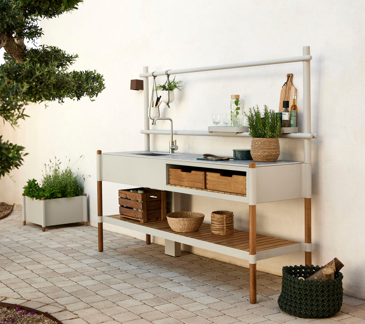 Modern kitchen unit featuring a metal basin, wooden shelves, and decorative plants in stylish containers. Clean design with natural elements.