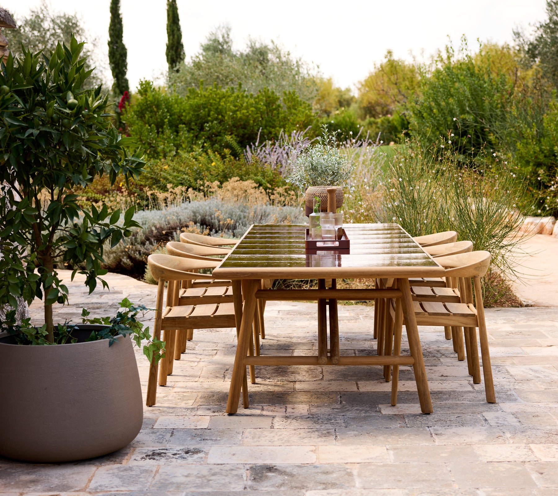 Modern outdoor dining table with wooden chairs in a garden setting.