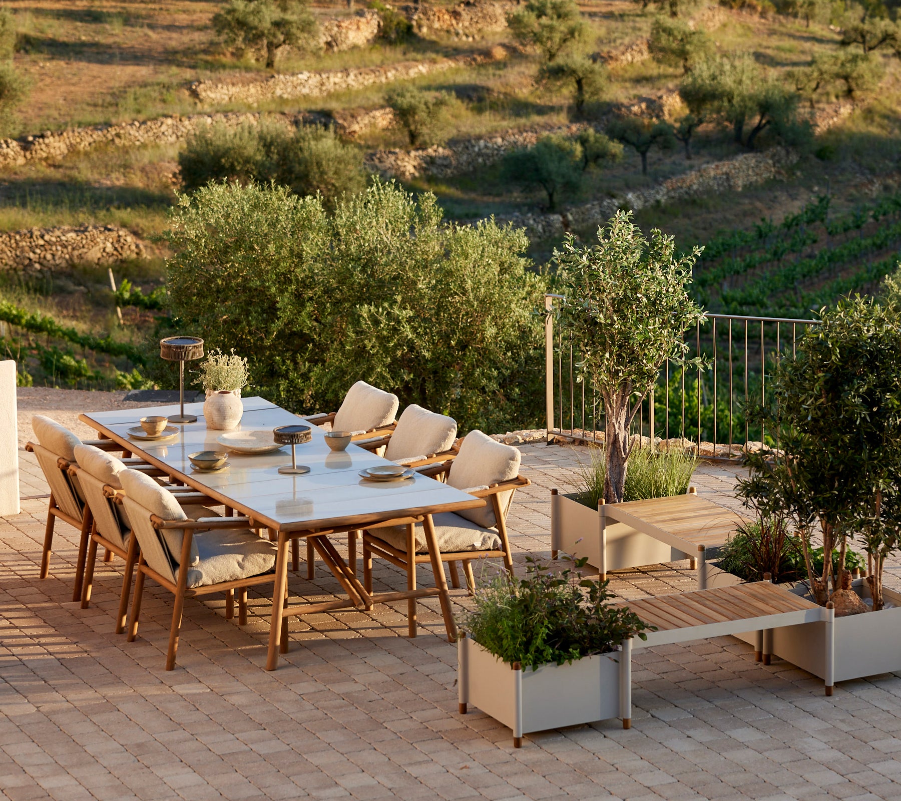 A stylish dining set with teak accents, featuring comfortable chairs and a planter bench, surrounded by greenery.