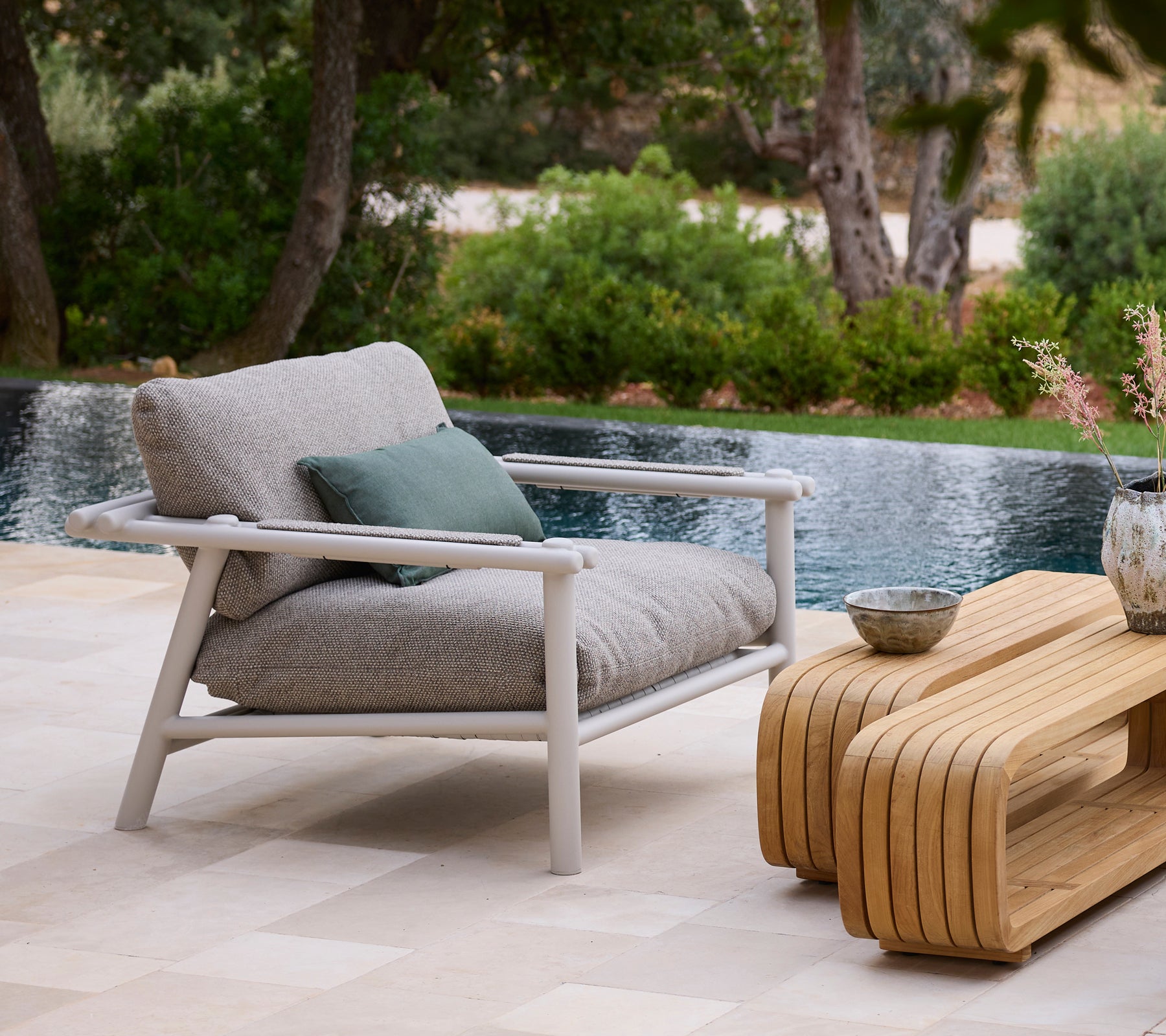 Modern outdoor setting with a grey sofa, green cushion, and wooden coffee table by a pool.