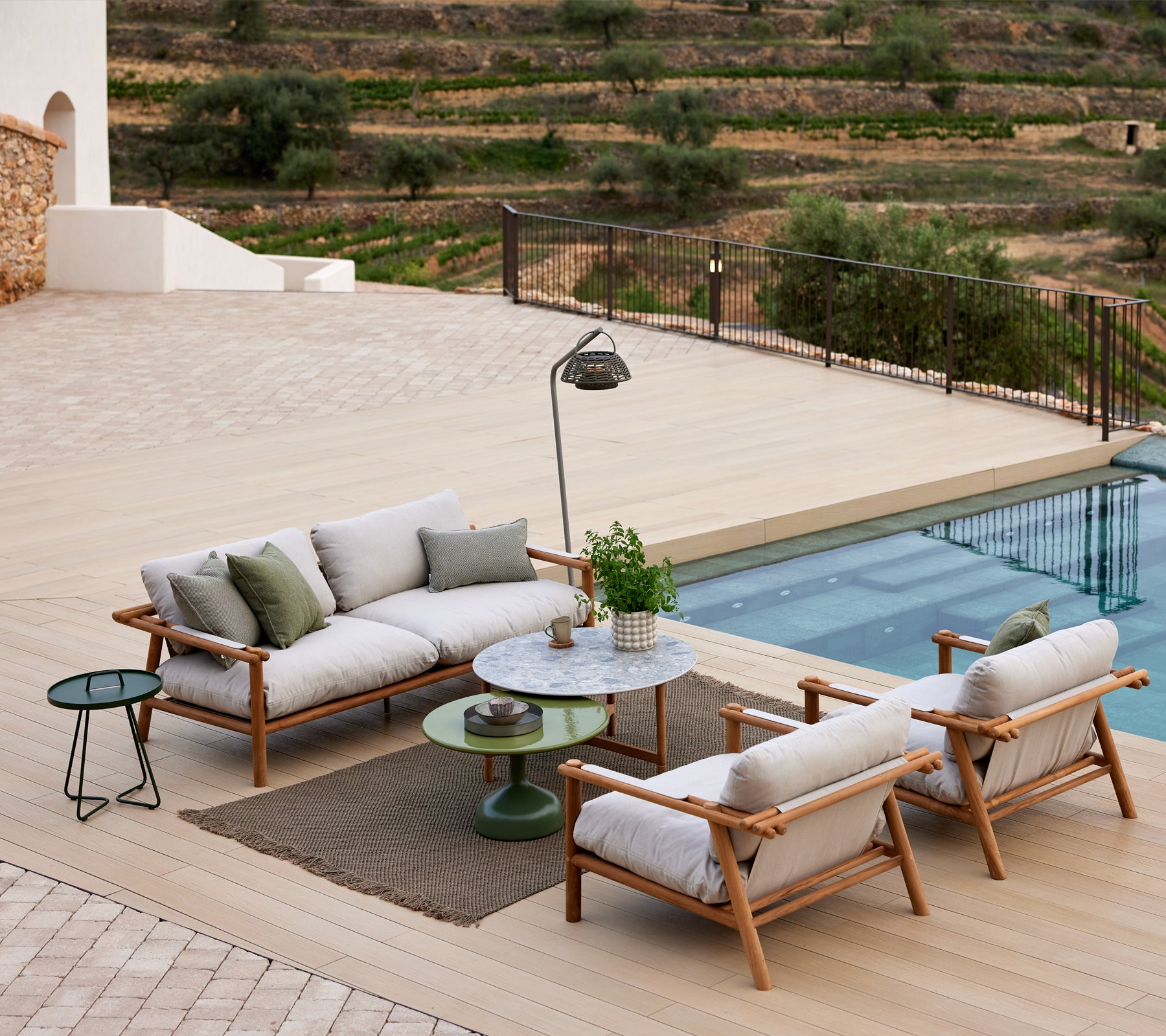 A lounge set featuring teak sticks, upholstered in knit fabric, alongside a glazed table, surrounded by a serene landscape.