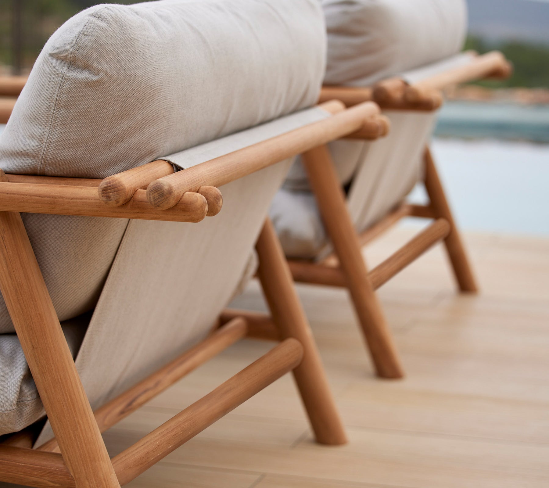 Two stylish lounge chairs featuring teak frames and comfortable beige cushions, showcasing a unique stick design on the backrest.
