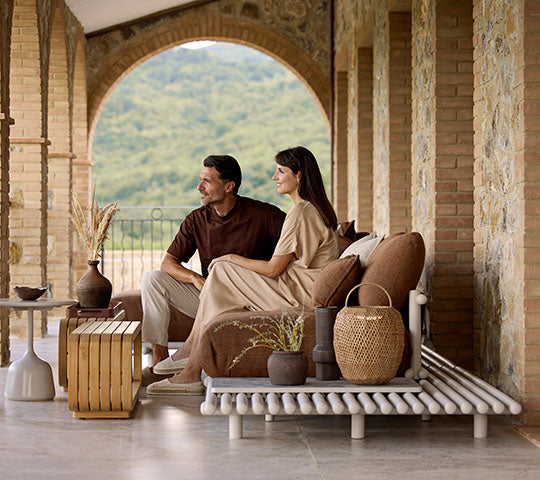 A couple sits together on a stylish sofa, complemented by a coffee table, decorative vases, and an elegant hanging lamp.