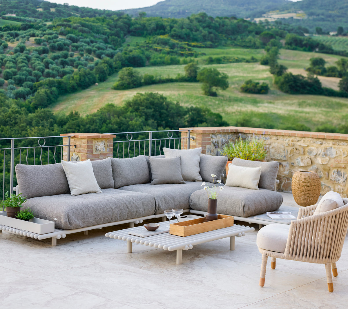 Stylish lounge area featuring a grey sectional sofa and a comfortable chair, set against a scenic landscape.