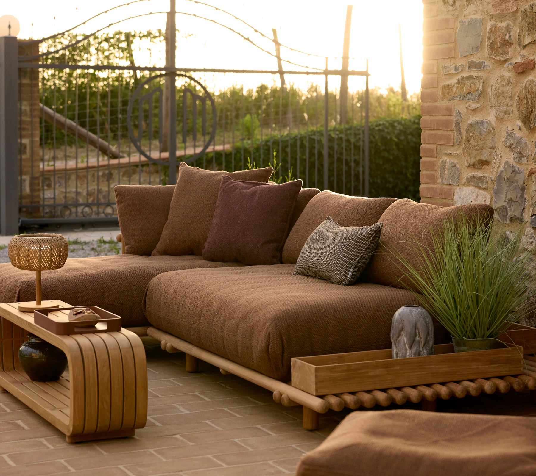 Mellow coffee table and teak club storage box beside a cozy outdoor seating area with cushions and plants in warm evening light.