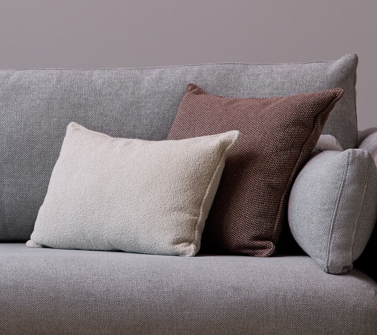 A white Scent scatter cushion and a Wove dark bordeaux cushion are placed on a gray sofa.