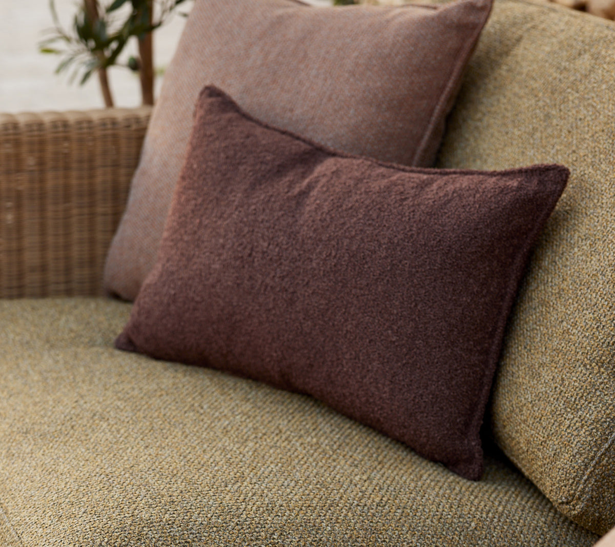Soft decorative cushions in earthy tones, arranged comfortably on a woven surface, adding a cozy touch to the setting.